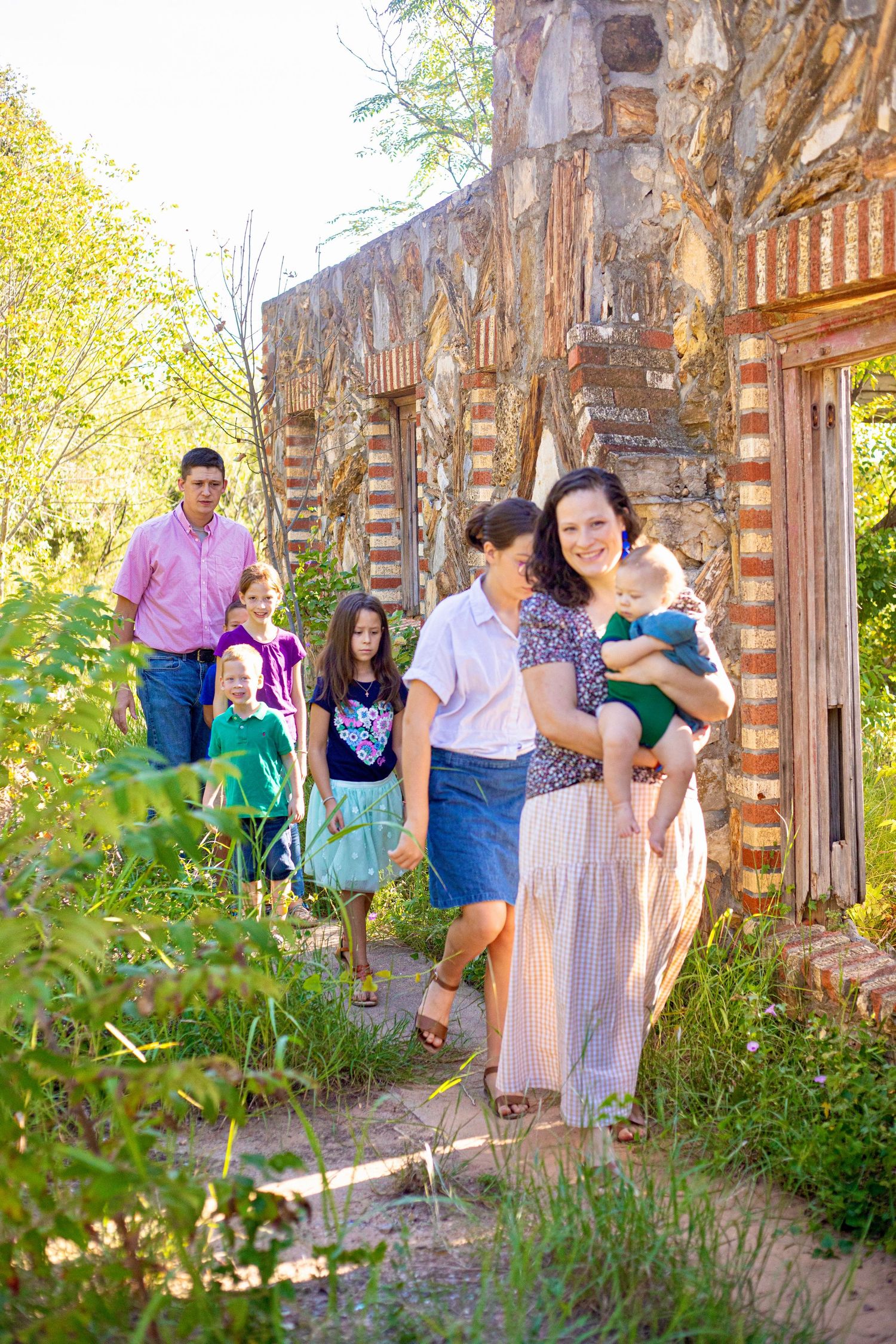 Family photo session by rustic stone wall with greenery and natural lighting.