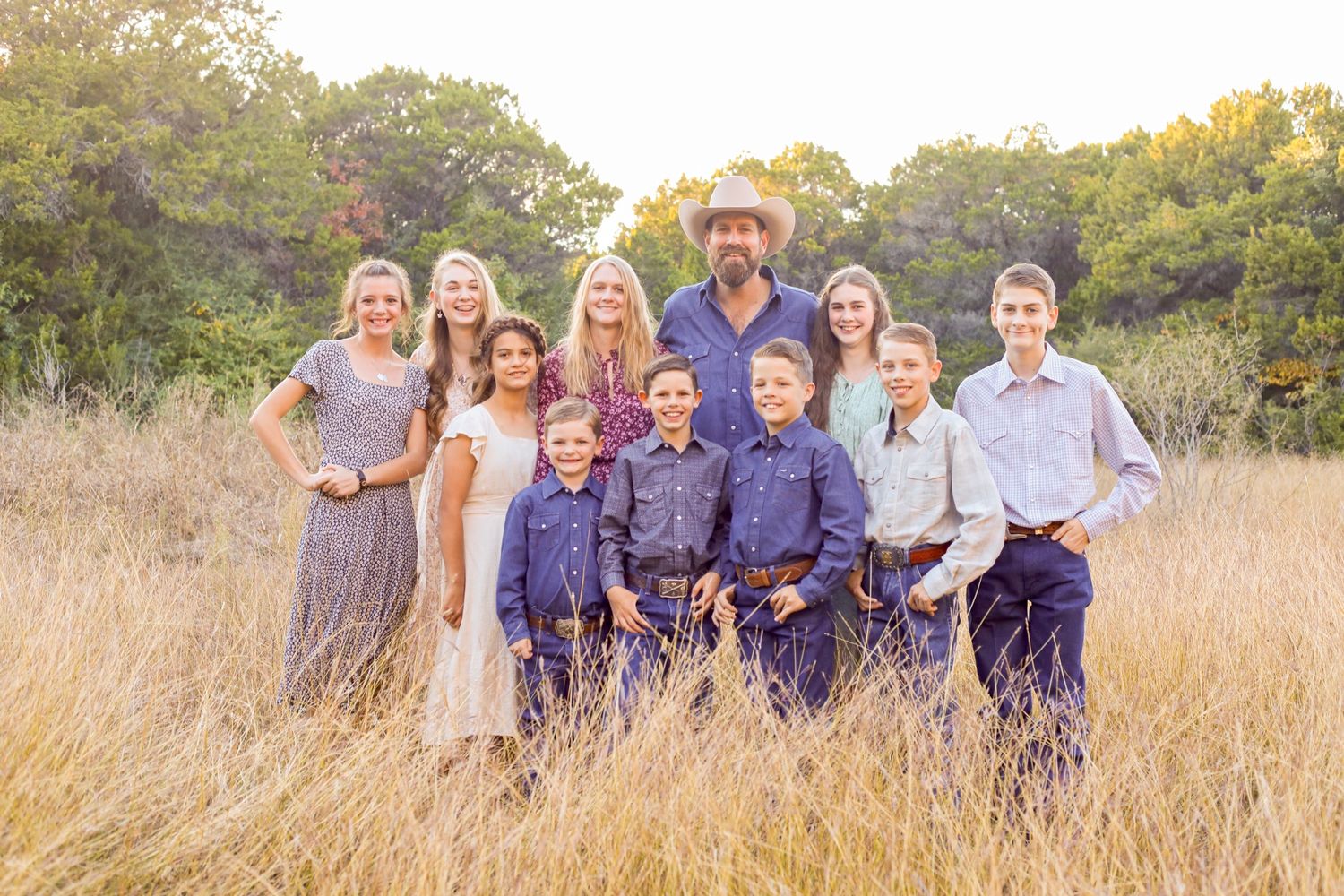 Extended family group photos taken in a sunlit field with coordinated blue and neutral outfits.