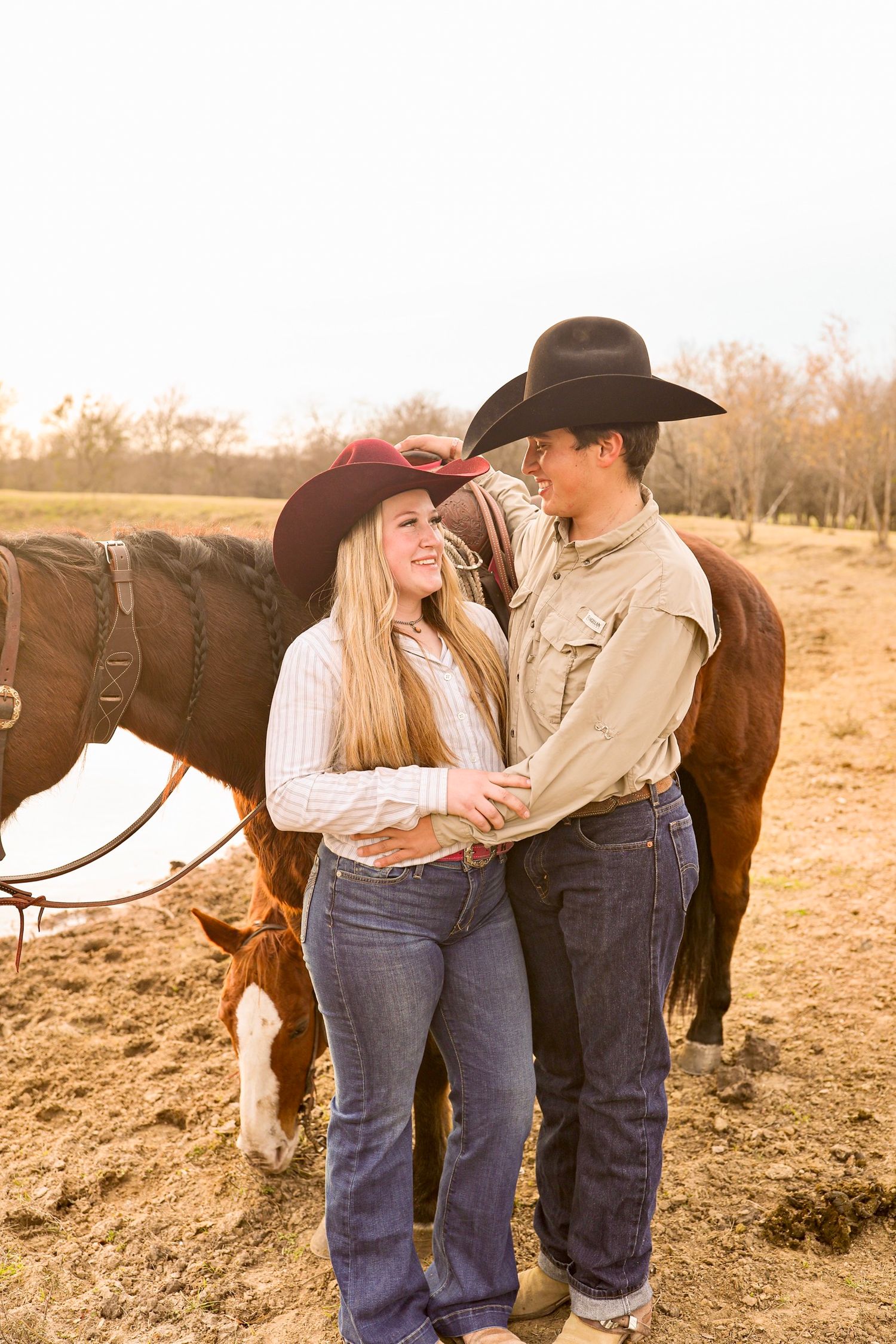 Couple in western wear shares tender moment beside horse at sunset.
