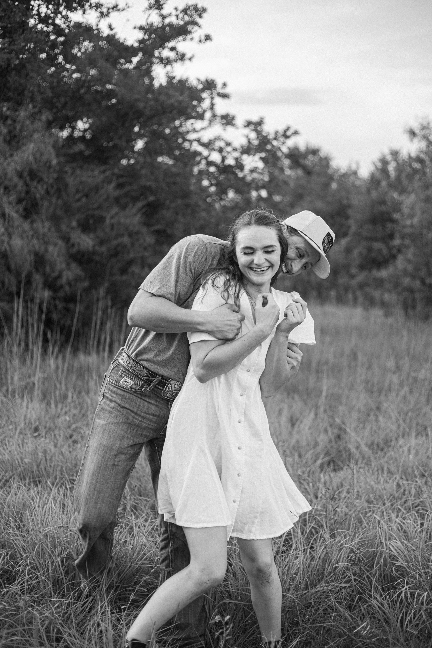 Black and white portrait of couple embracing in field.