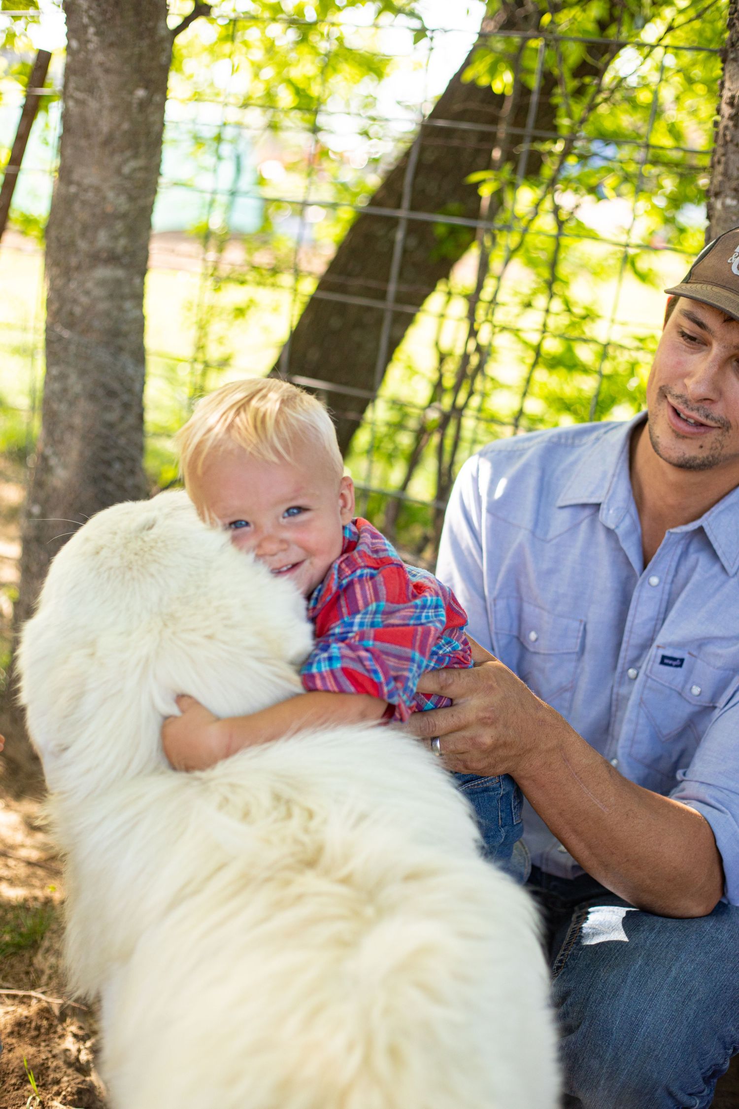 Family and fluffy white dog enjoy a sunny day outdoors in a wooded setting.