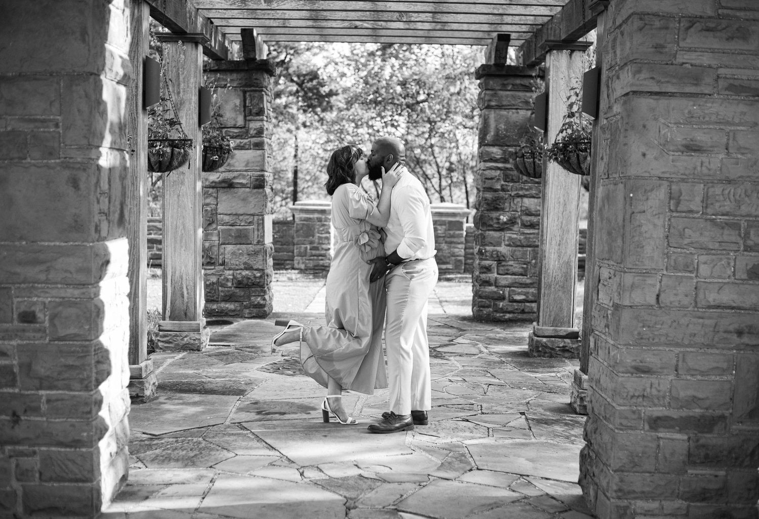 A black and white photo of a romantic moment under an architectural pergola.