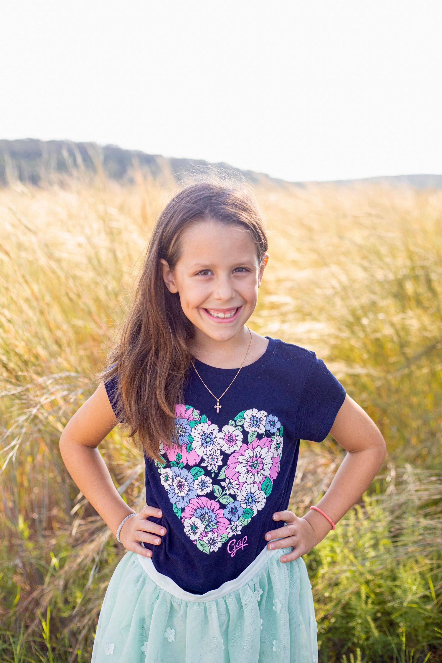 A young person in a navy floral shirt and mint skirt poses in a wheat field.