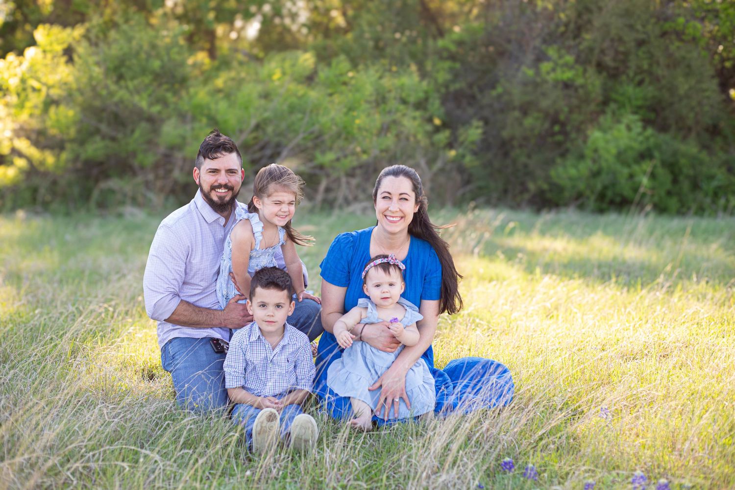 Happy family of five posing together in a sunny green meadow for an outdoor portrait session.