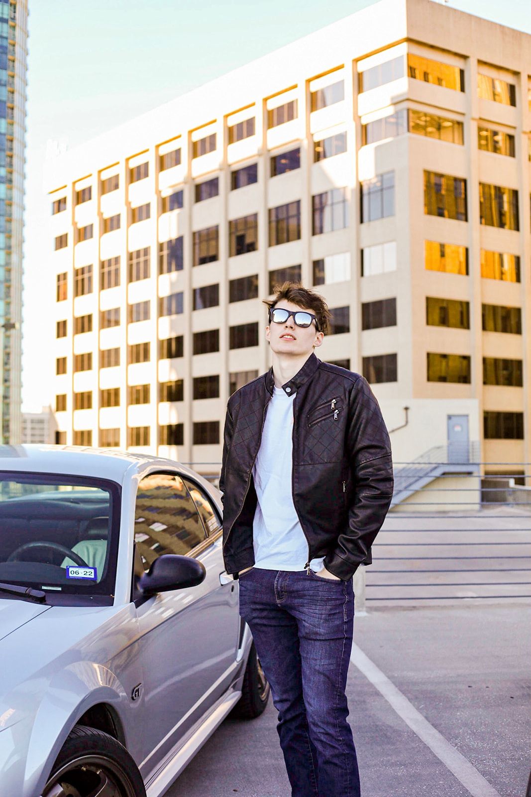 Fashion photoshoot featuring casual wear and a silver car in an urban parking structure.