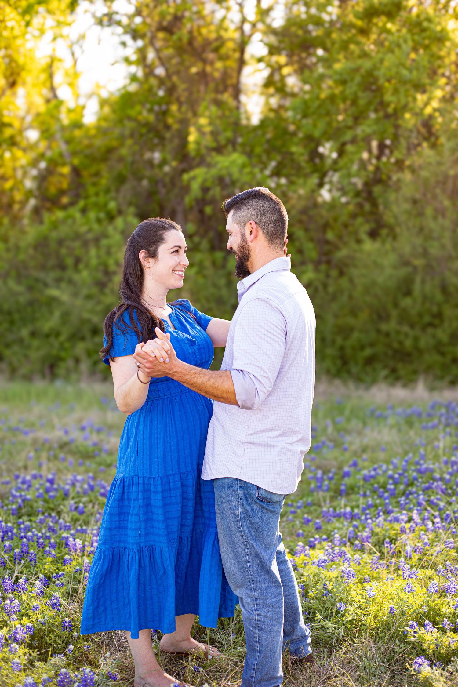Couple dancing in a Texas bluebonnet field, woman in blue dress, man in white shirt and jeans, golden hour.