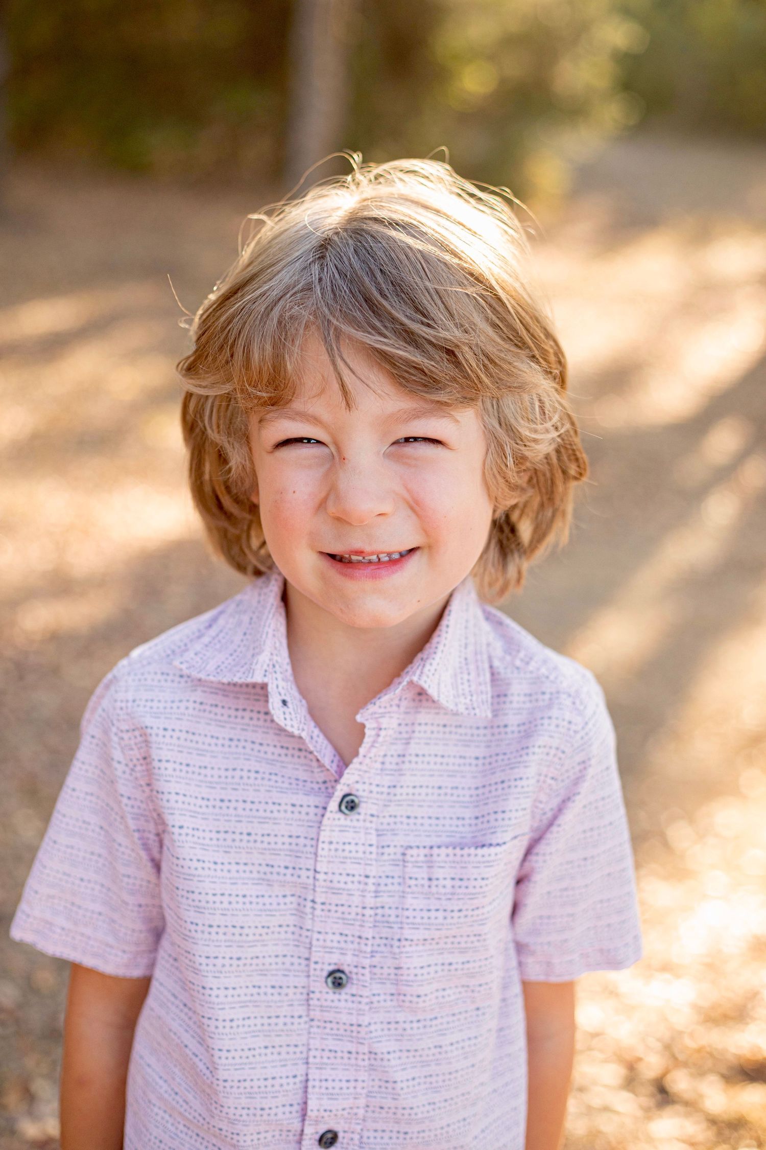 A child wearing a pink button-up shirt smiles brightly in golden outdoor lighting.