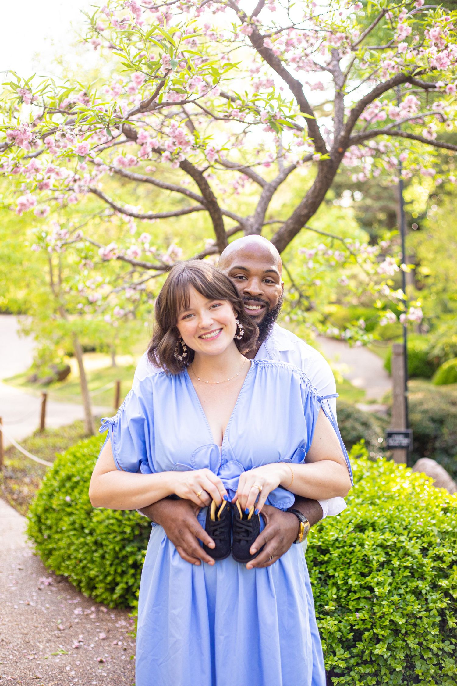 A couple embracing in a spring garden with blooming cherry blossoms and manicured shrubs.