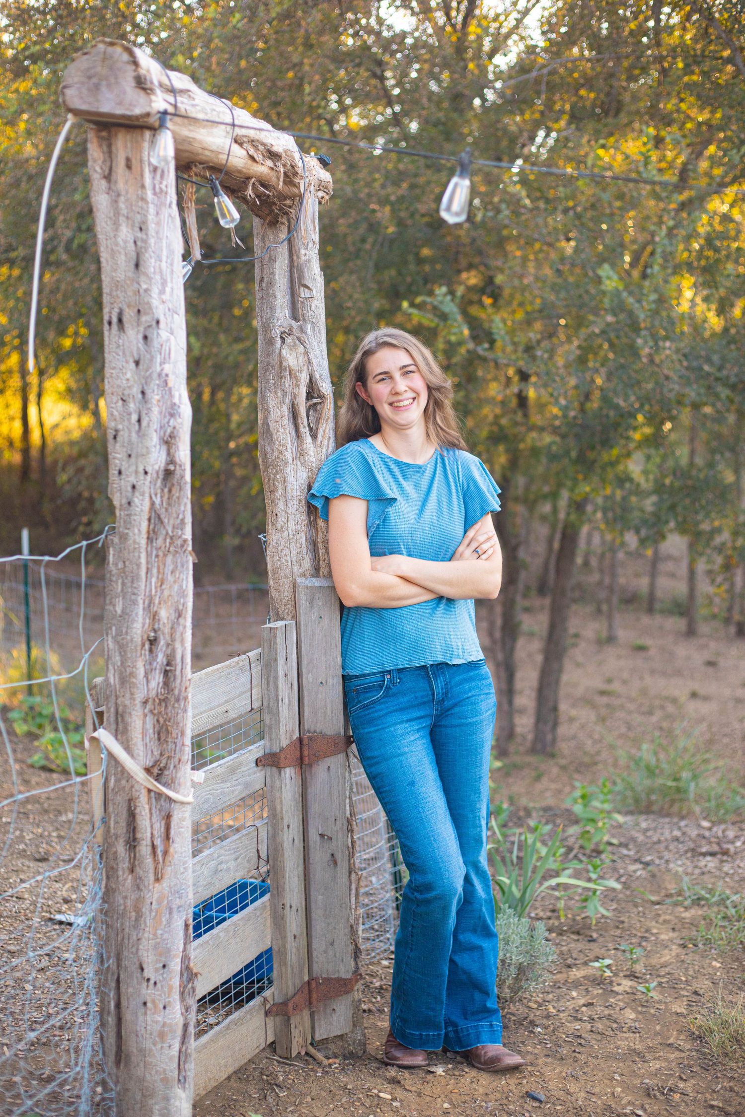 Person in blue top and jeans standing by rustic wooden gate structure.