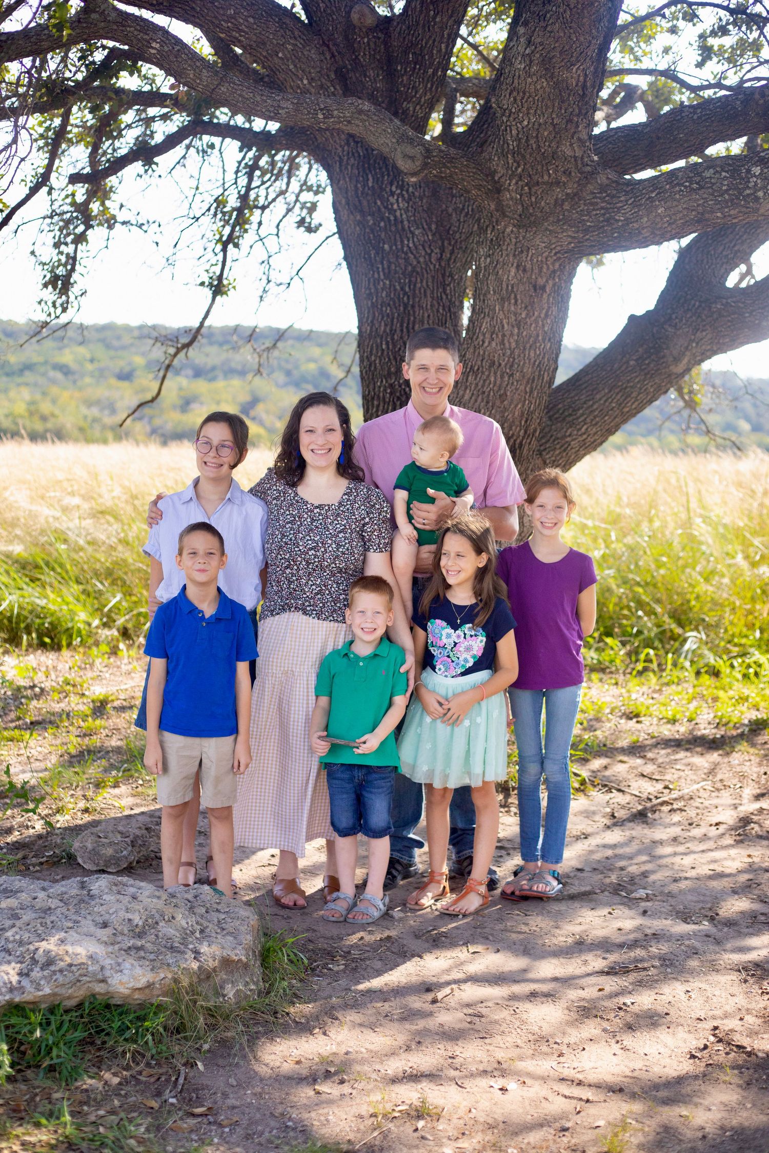 Group portrait under a sprawling tree with mountains visible in the distance.