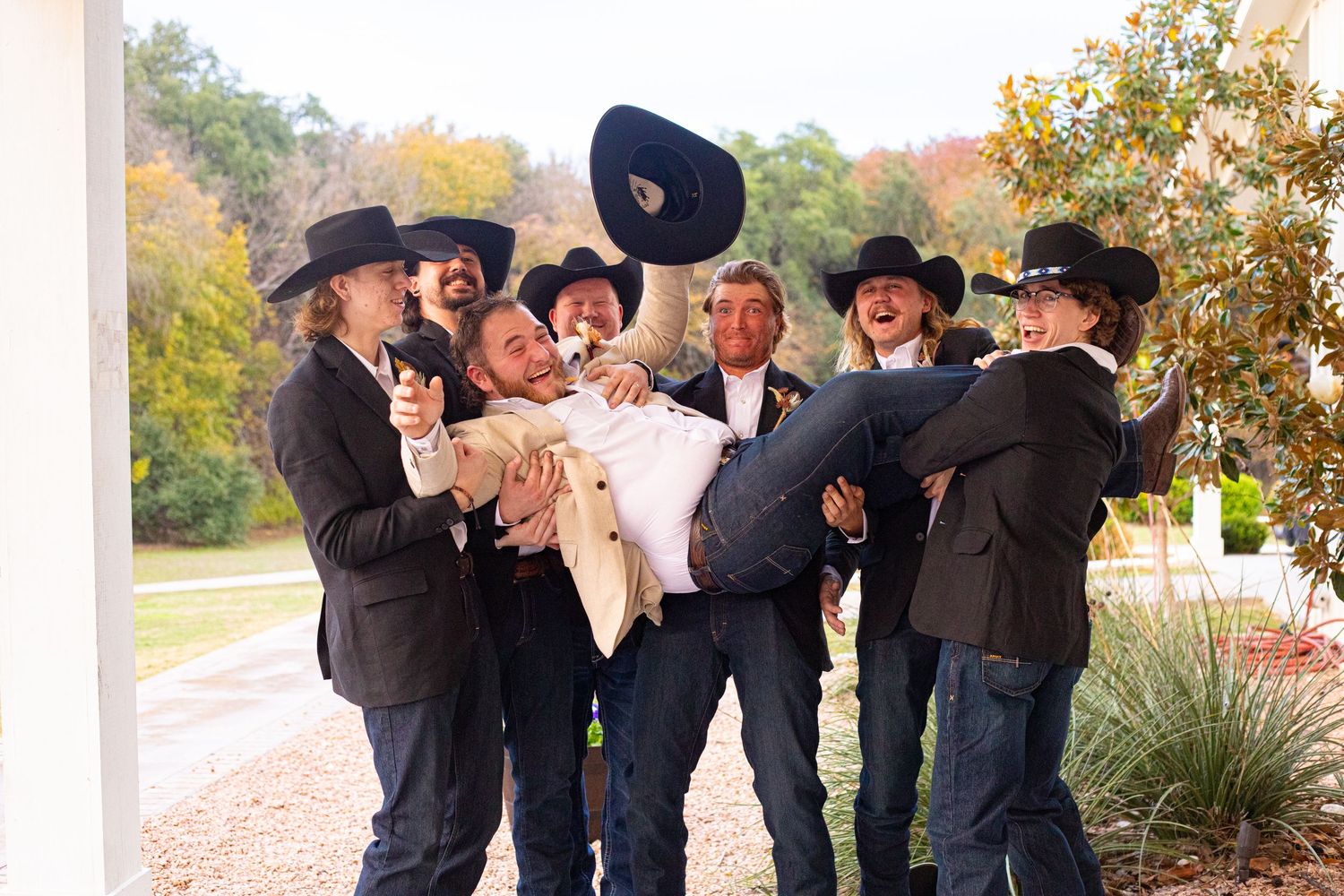 Groomsmen in dark attire and cowboy hats pose playfully for group photo.