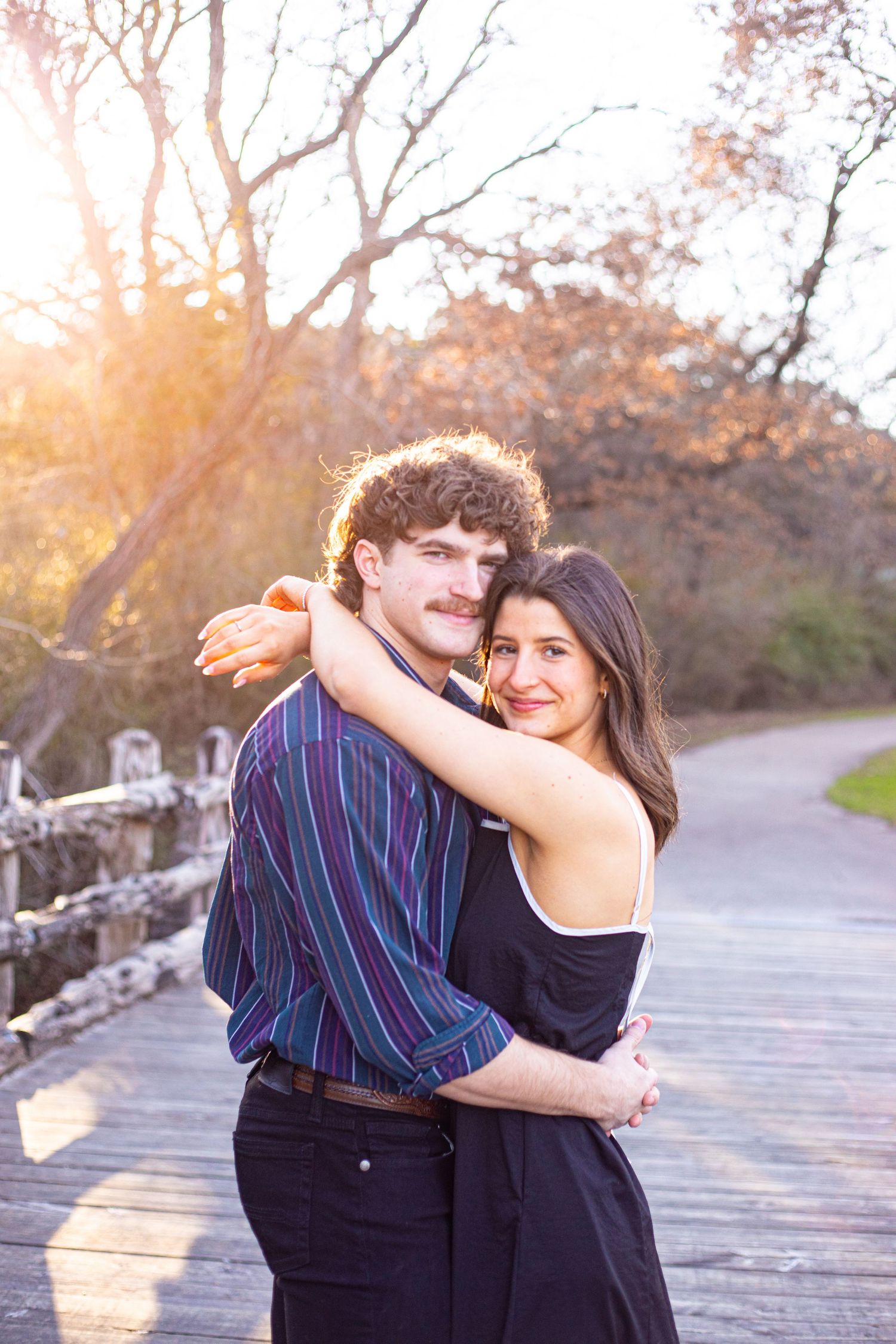 A couple embraces on a wooden boardwalk during golden hour.