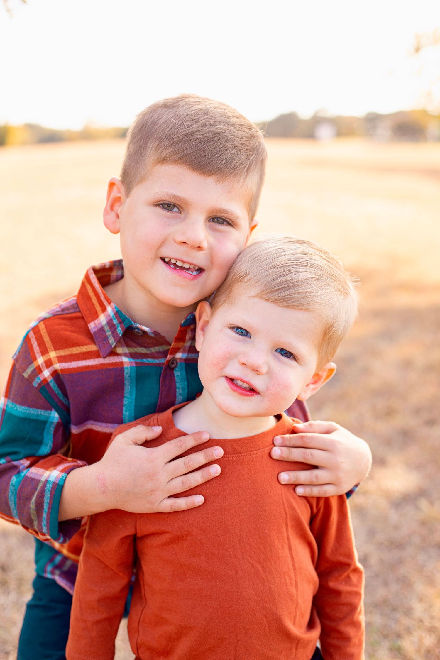 Sweet sibling interaction captured in warm sunset light with natural outdoor background.