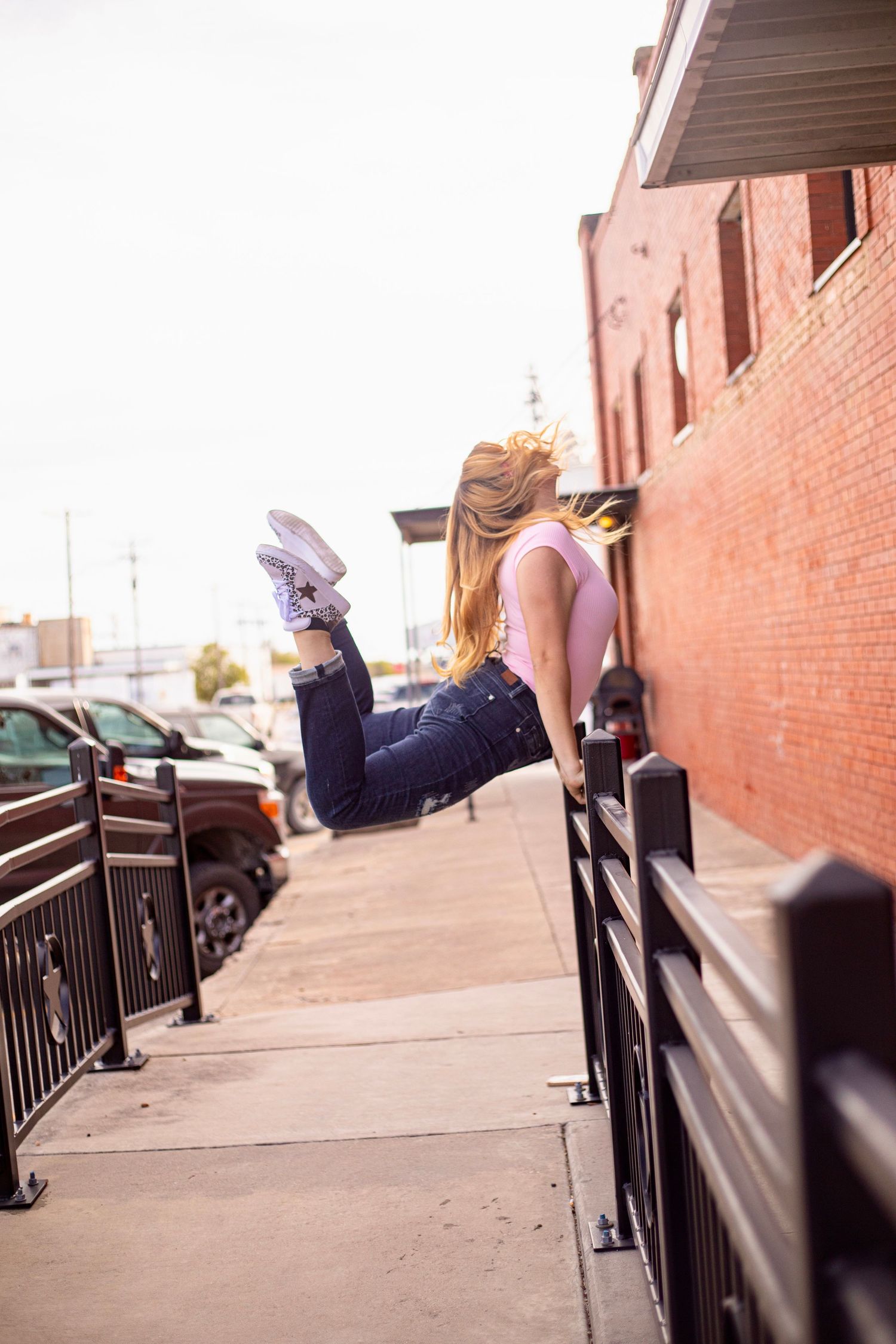 Creative urban photo showing someone sitting on metal railings against brick building backdrop.