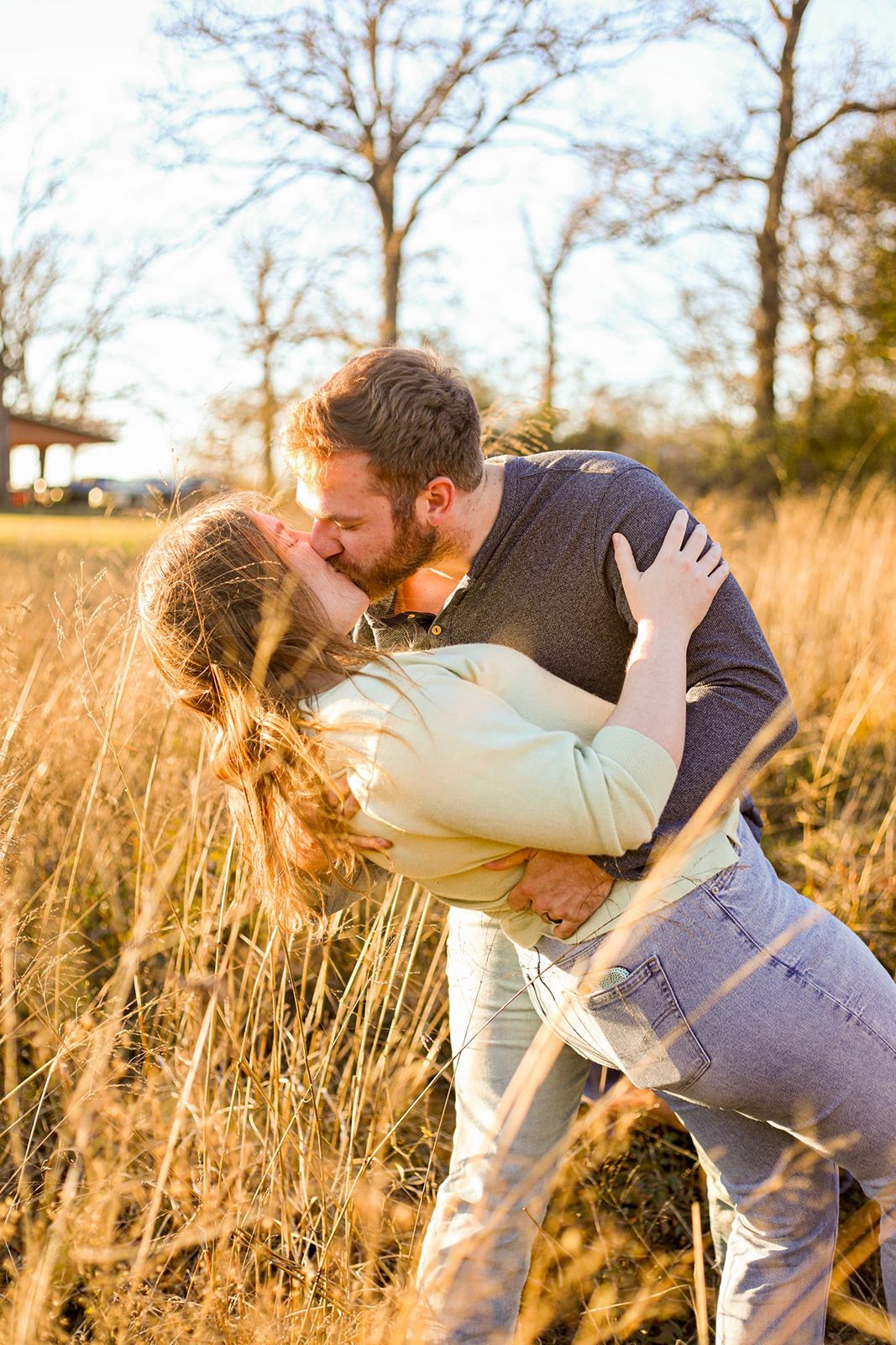 Couple shares romantic dip kiss in golden field at sunset.