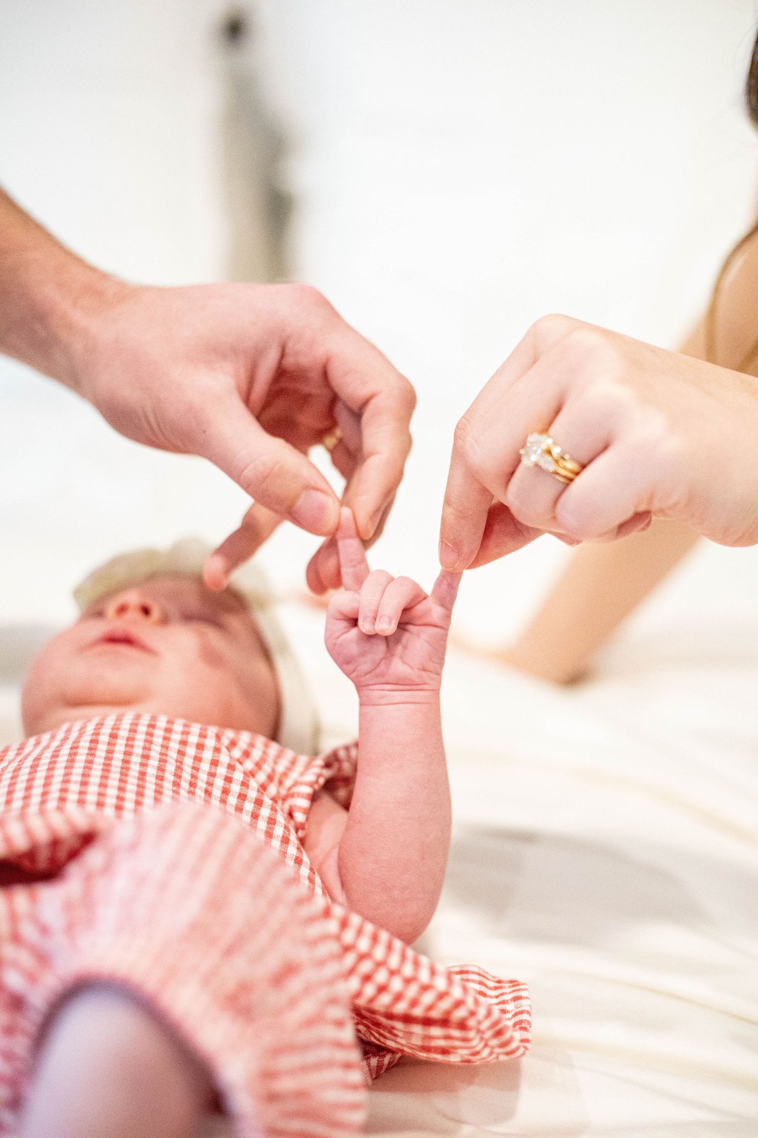 Newborn baby in red outfit grasping parents' fingers, close-up of tiny hand held by mother and father.