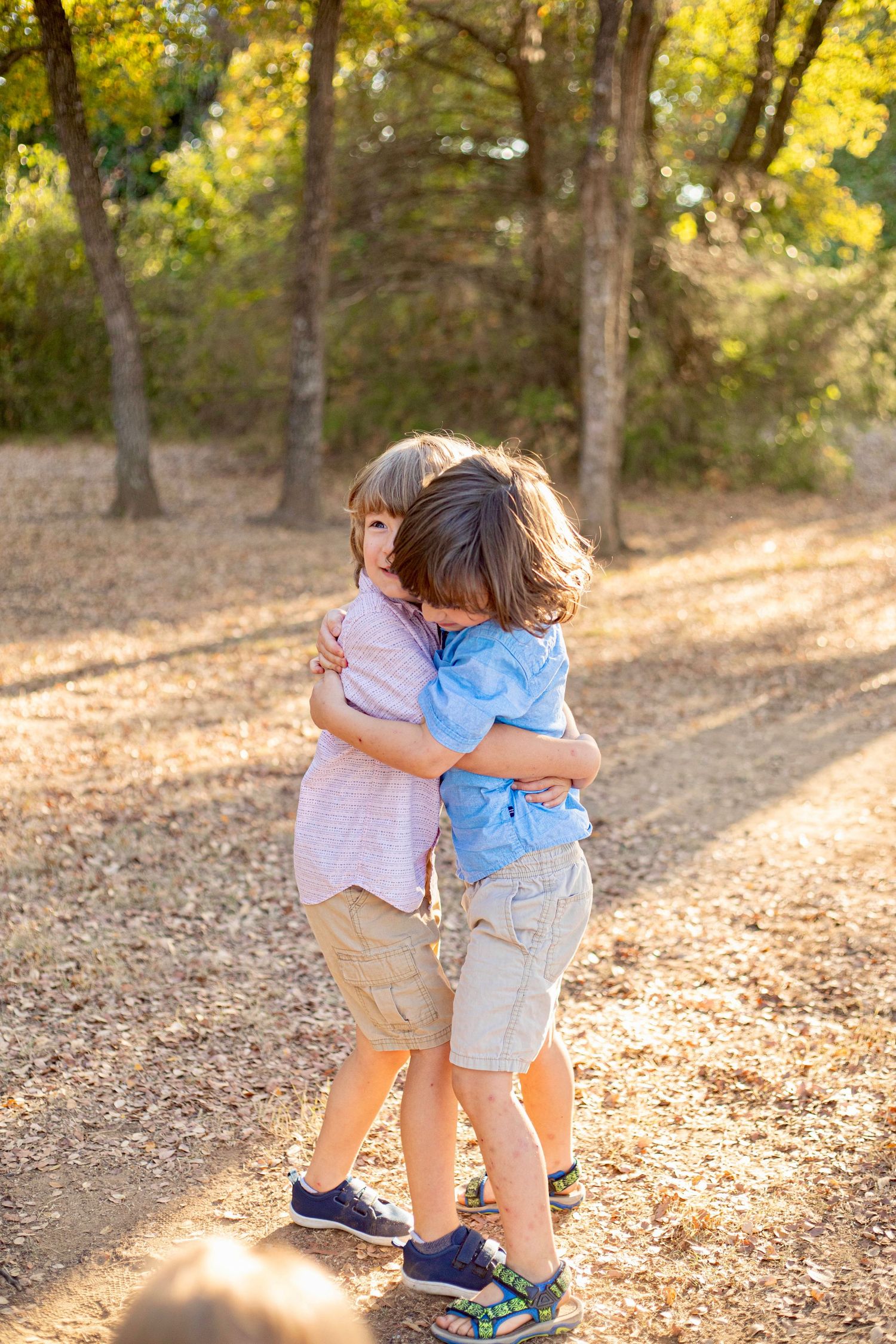 Two children hugging and playing together on a leaf-covered forest path in autumn.