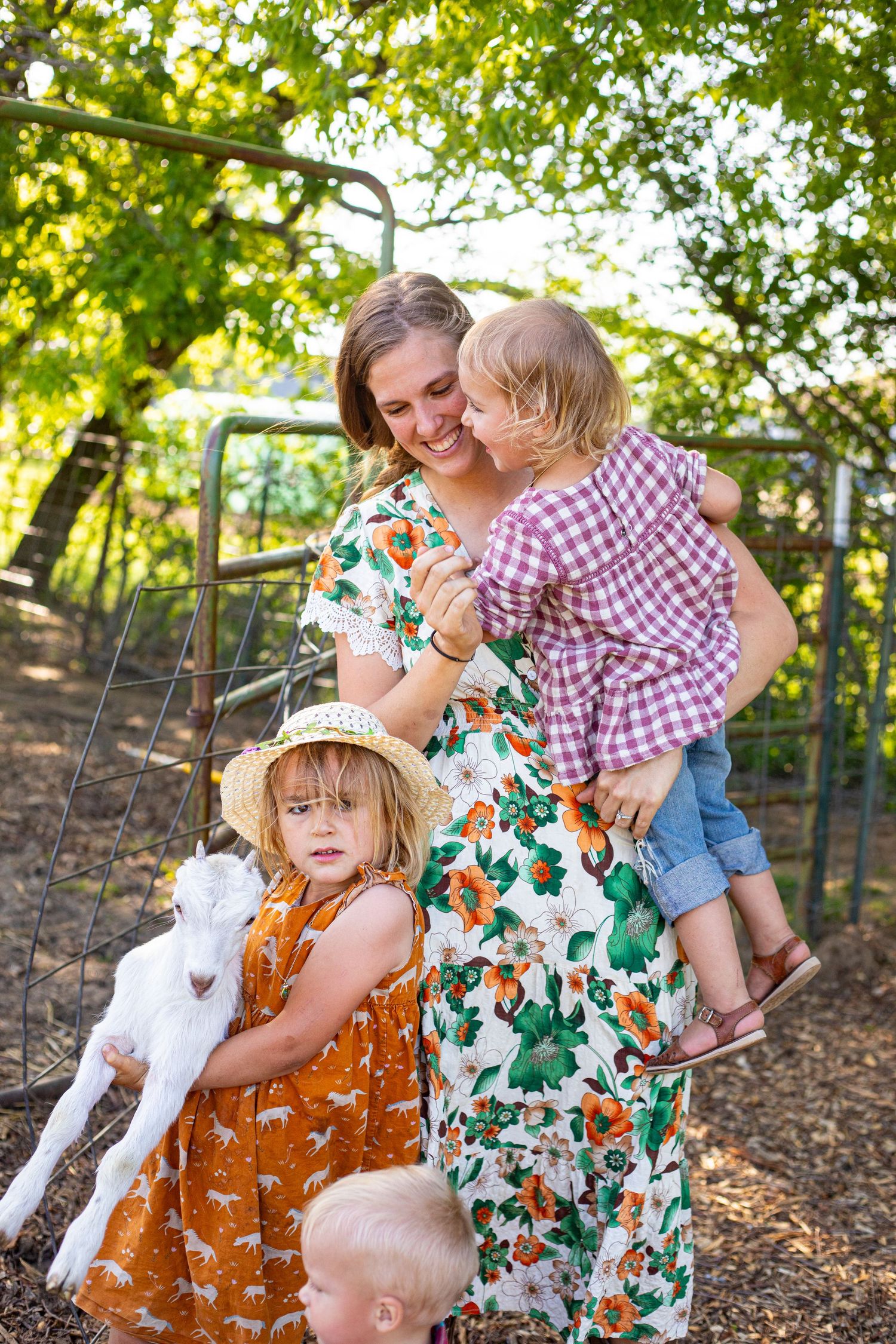 Family spending time with white goats at a farm enclosure on a sunny day.