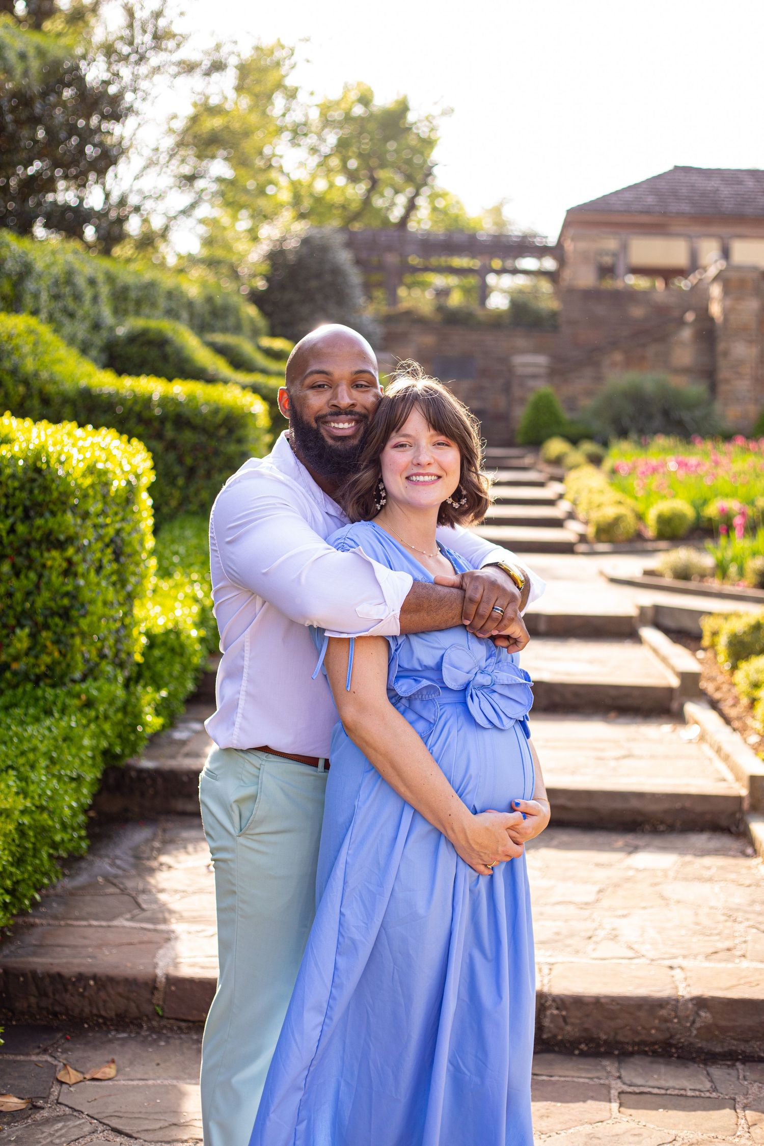 A couple sharing a tender moment on stone garden steps surrounded by manicured hedges.