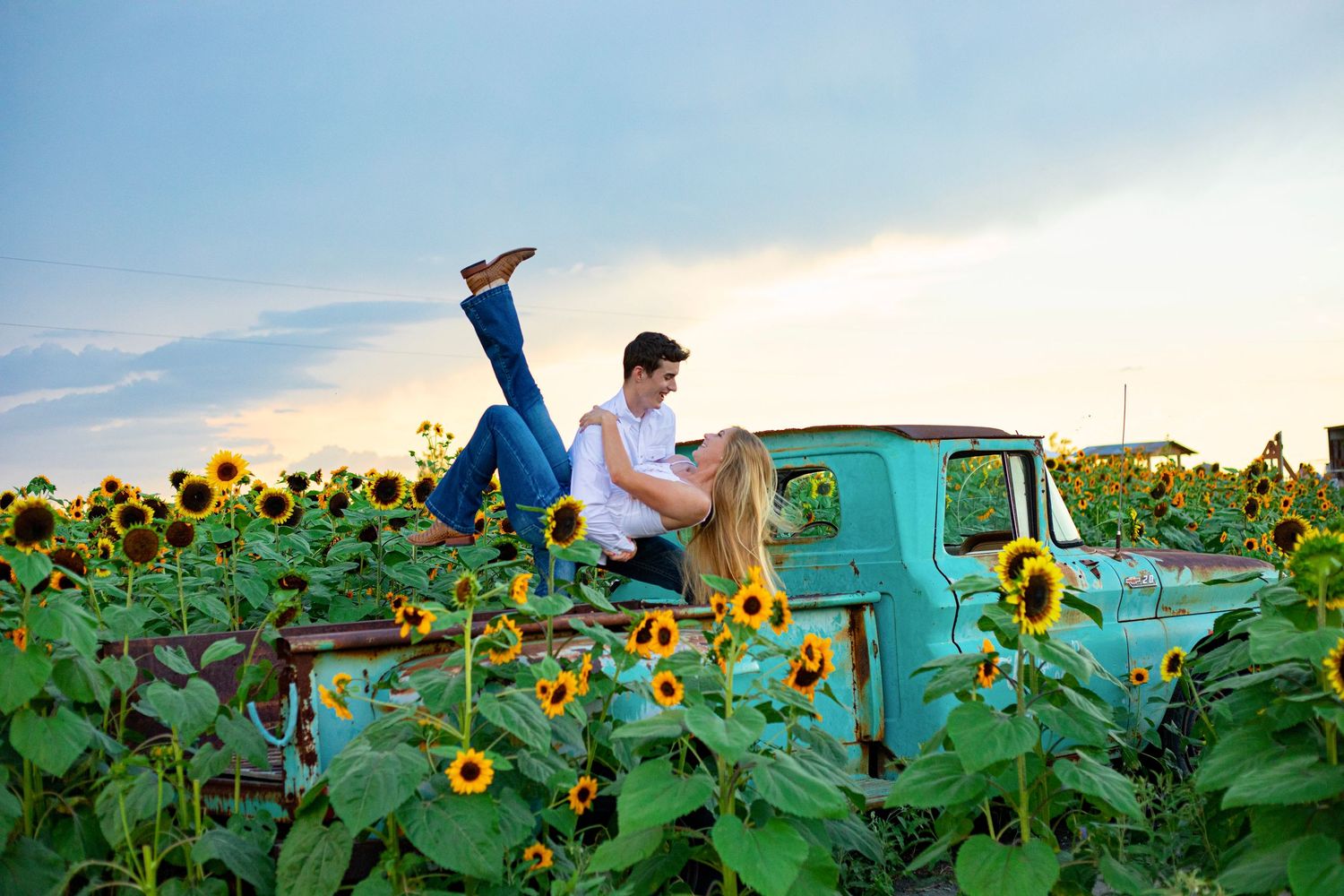 Couple posing playfully in vibrant sunflower field with vintage turquoise truck.