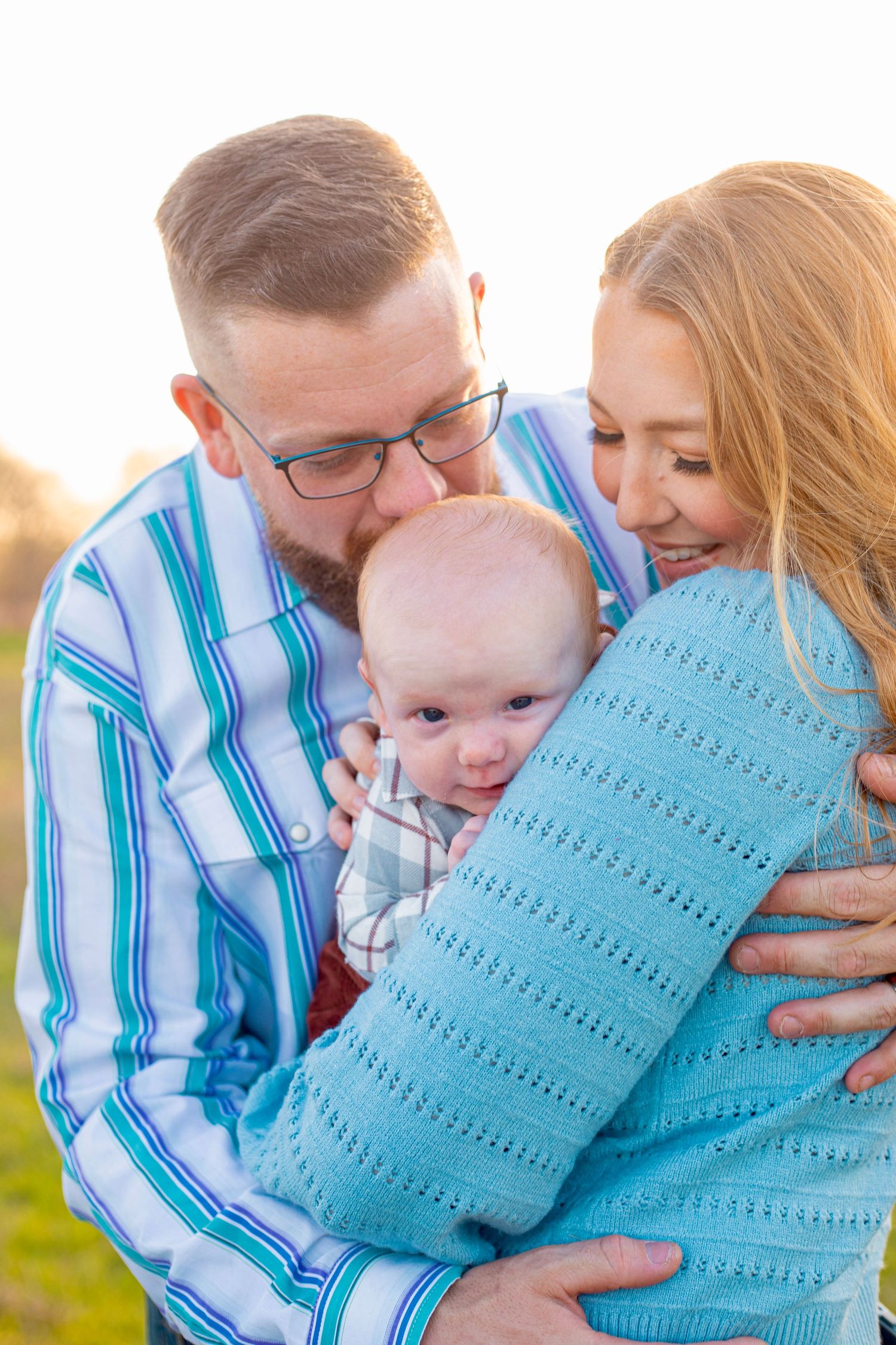Family shares tender moment with baby wrapped in turquoise blanket during sunset portrait session.