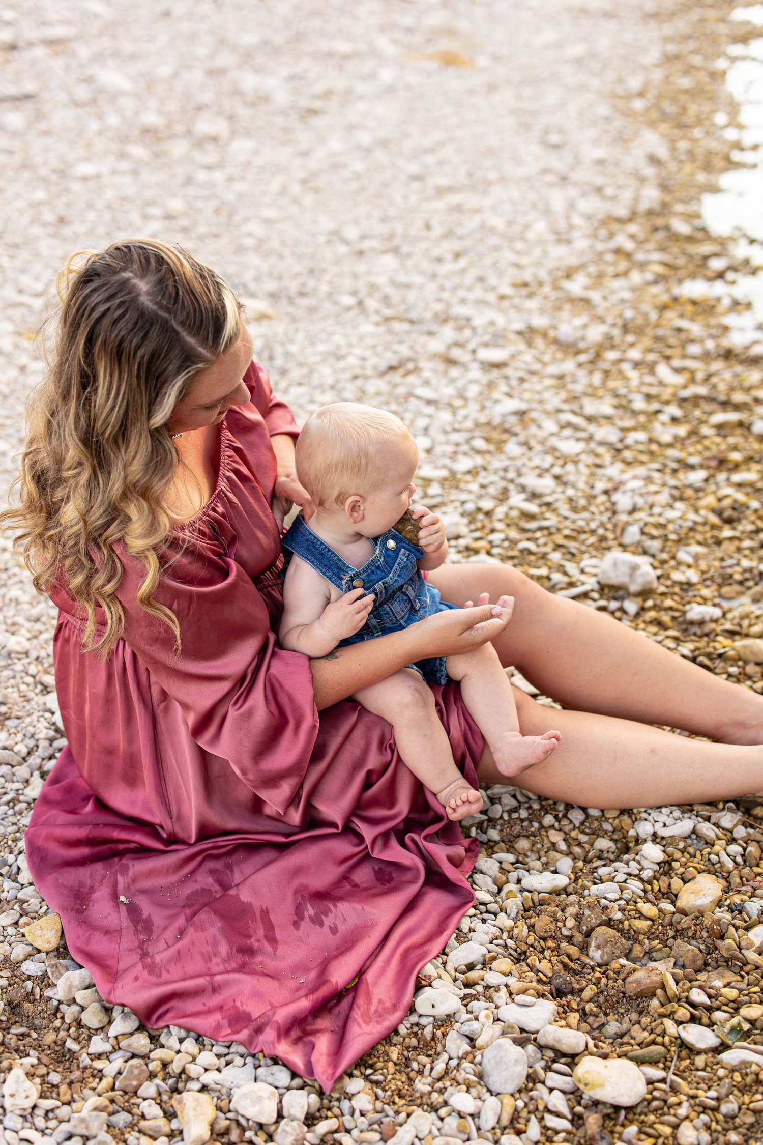Sitting on a rocky riverbank wearing a flowing pink dress while sharing a quiet moment together.