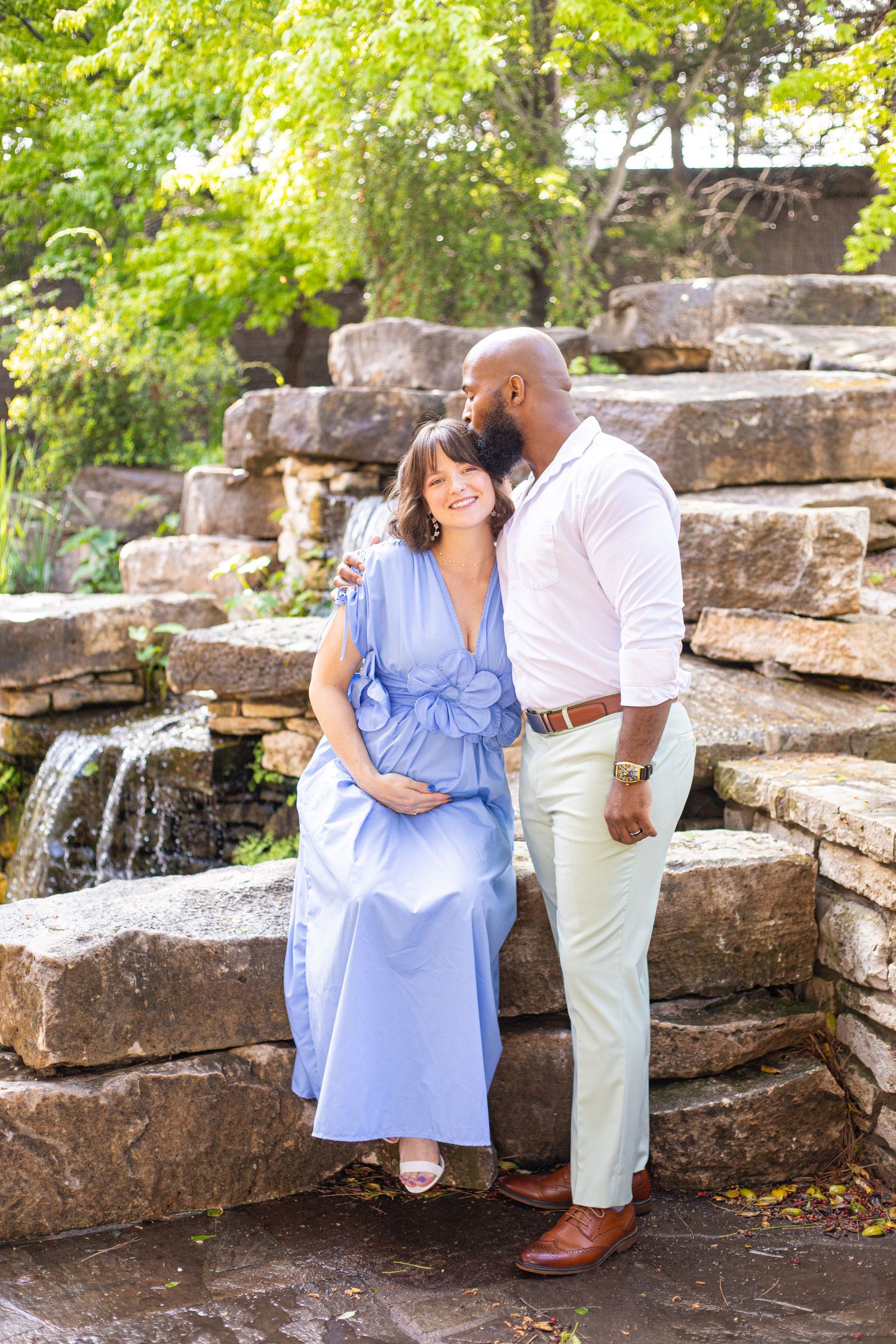 Couple posing by stone waterfall feature, person wearing flowing blue dress.