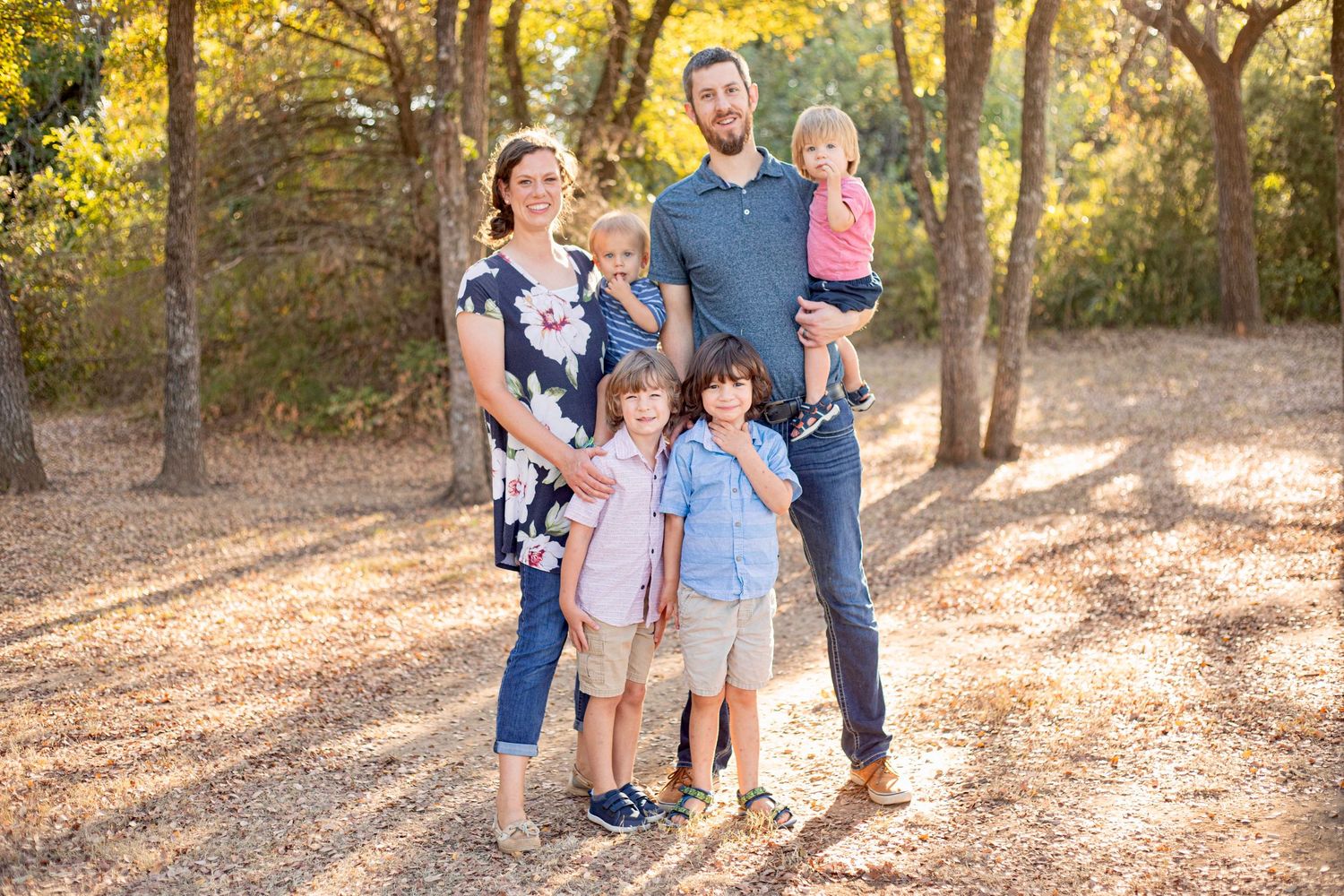 A family portrait in a wooded setting with warm autumn lighting filtering through trees.
