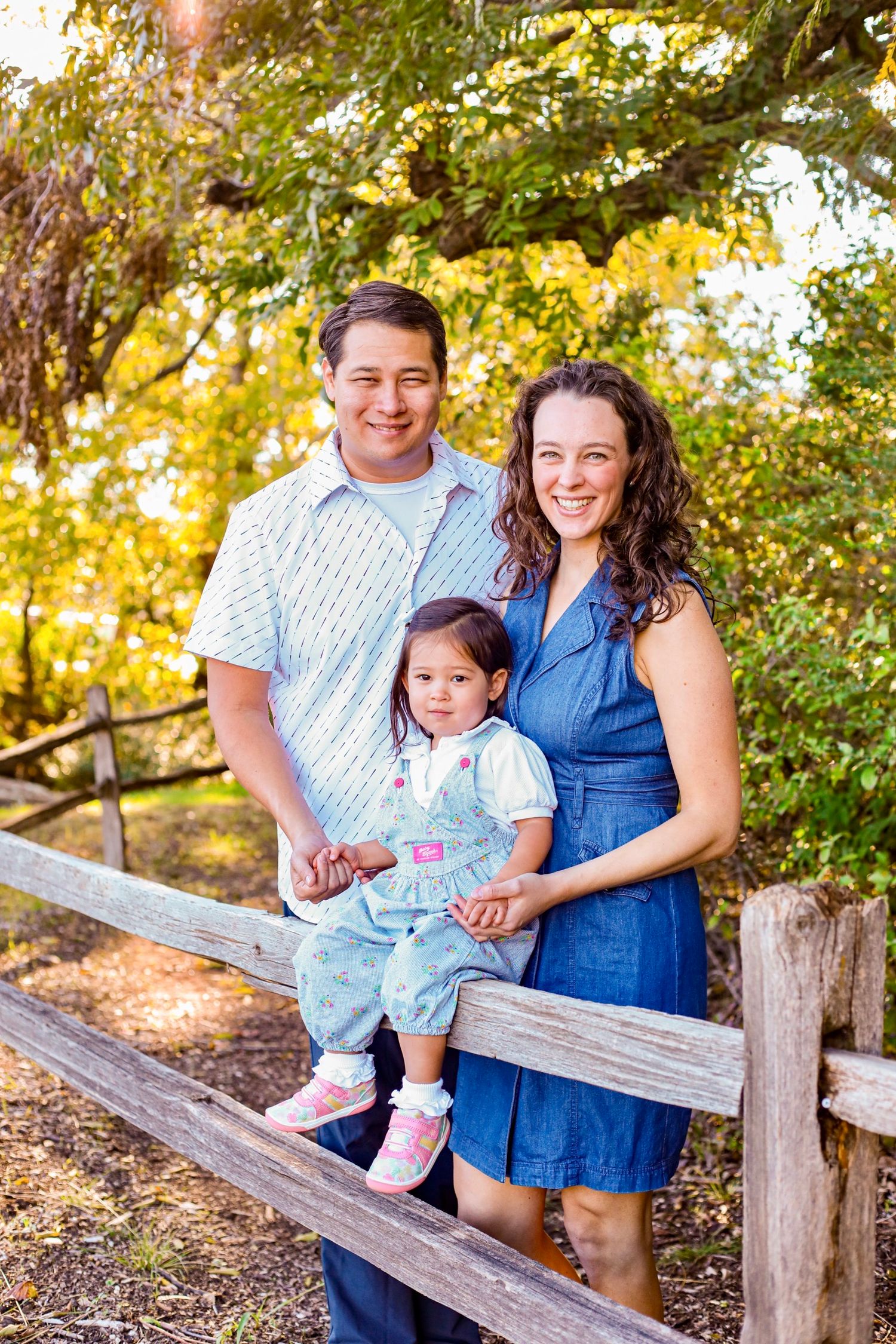 Family sitting together on a wooden bench surrounded by autumn foliage.