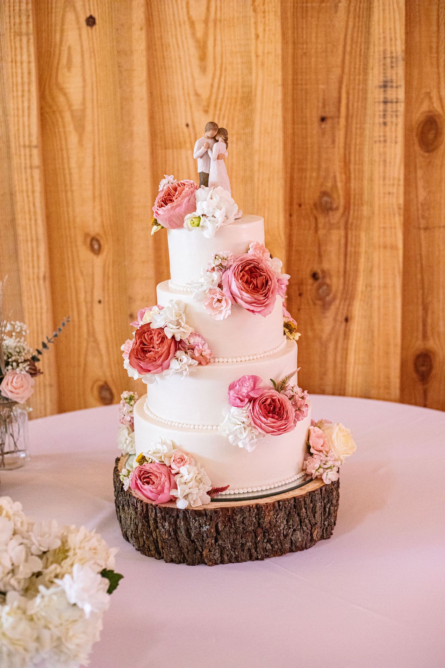 Two-tiered pink wedding cake decorated with fresh roses on rustic wood slice base.