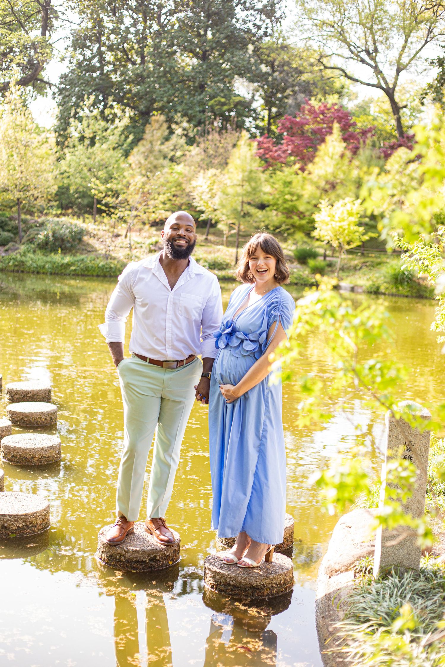 Couple sharing tender moment on stepping stones over pond in sunny garden setting.