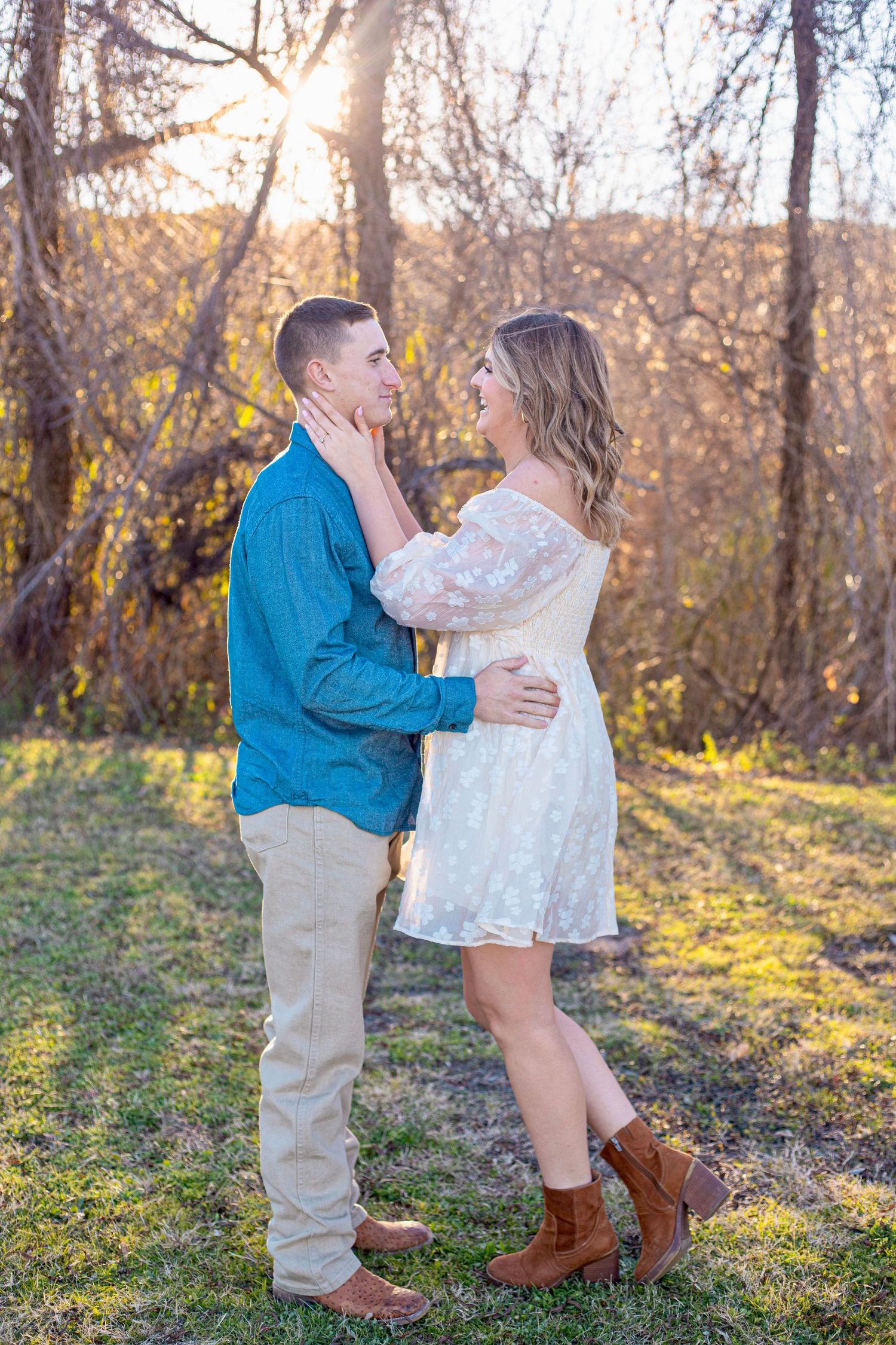 A couple shares an intimate moment while standing together during sunset with fall trees behind them.