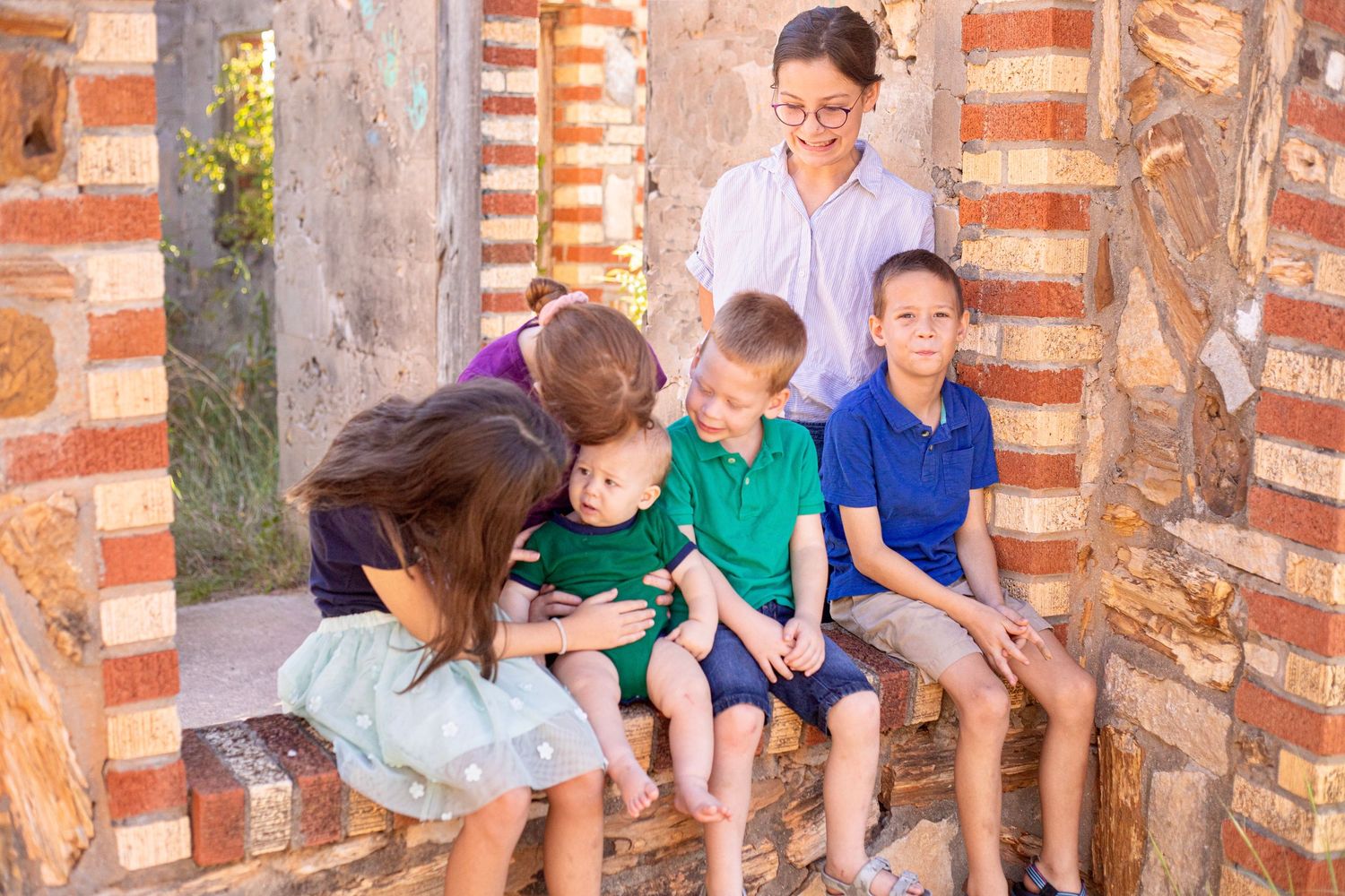 Group sitting together on brick ledge sharing laughs in front of weathered stone wall.