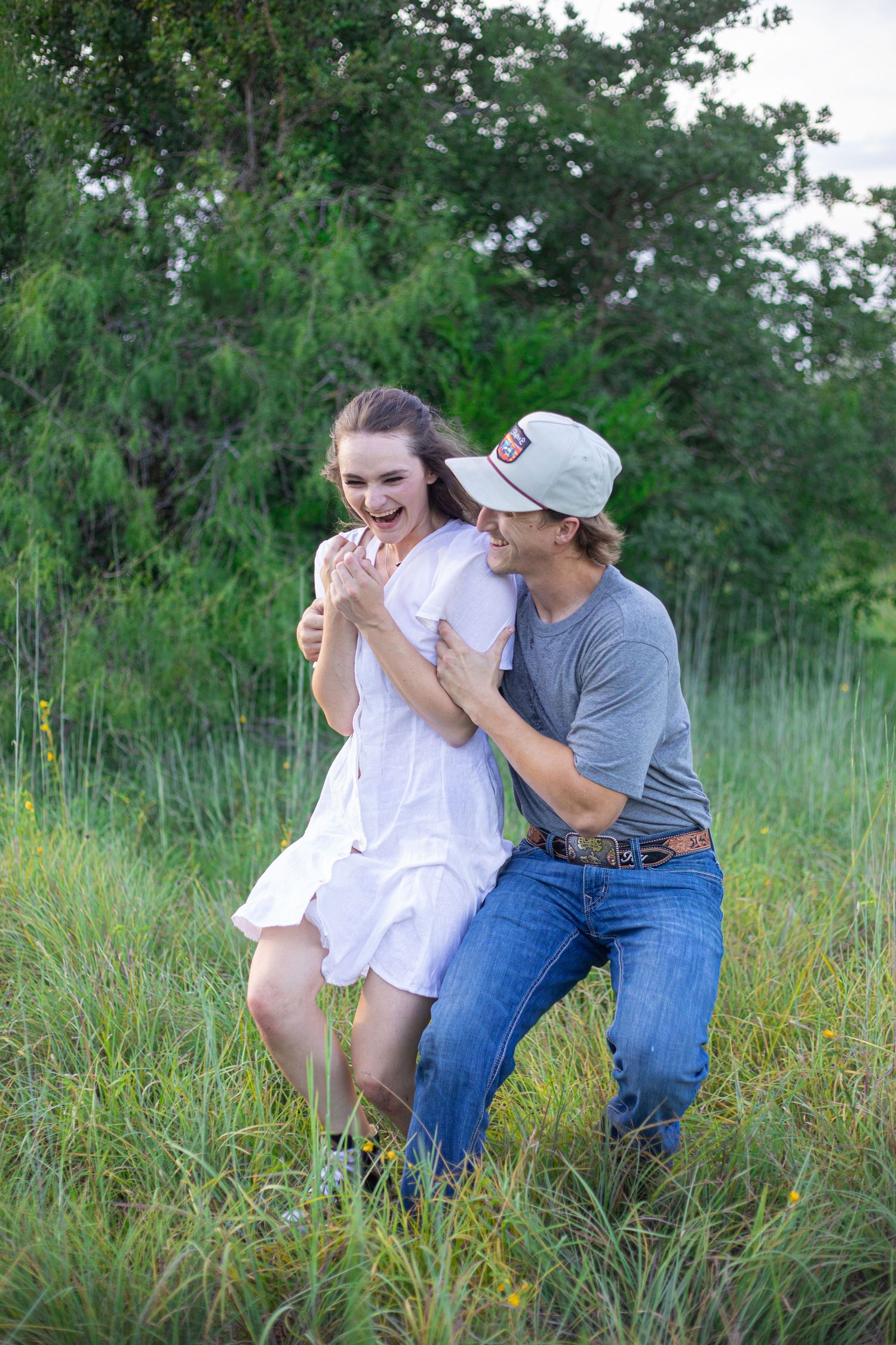 Couple laughing together in tall grass field during summer.