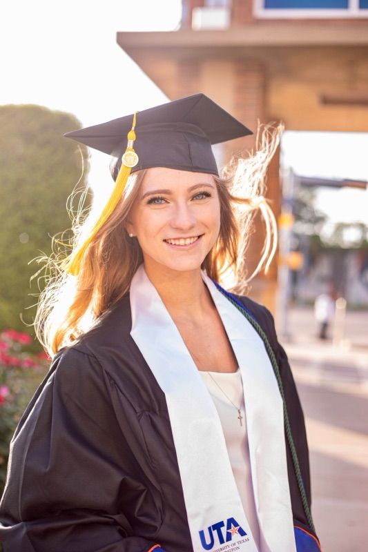 Graduate in traditional cap and gown with UTA stole during sunset photo session.
