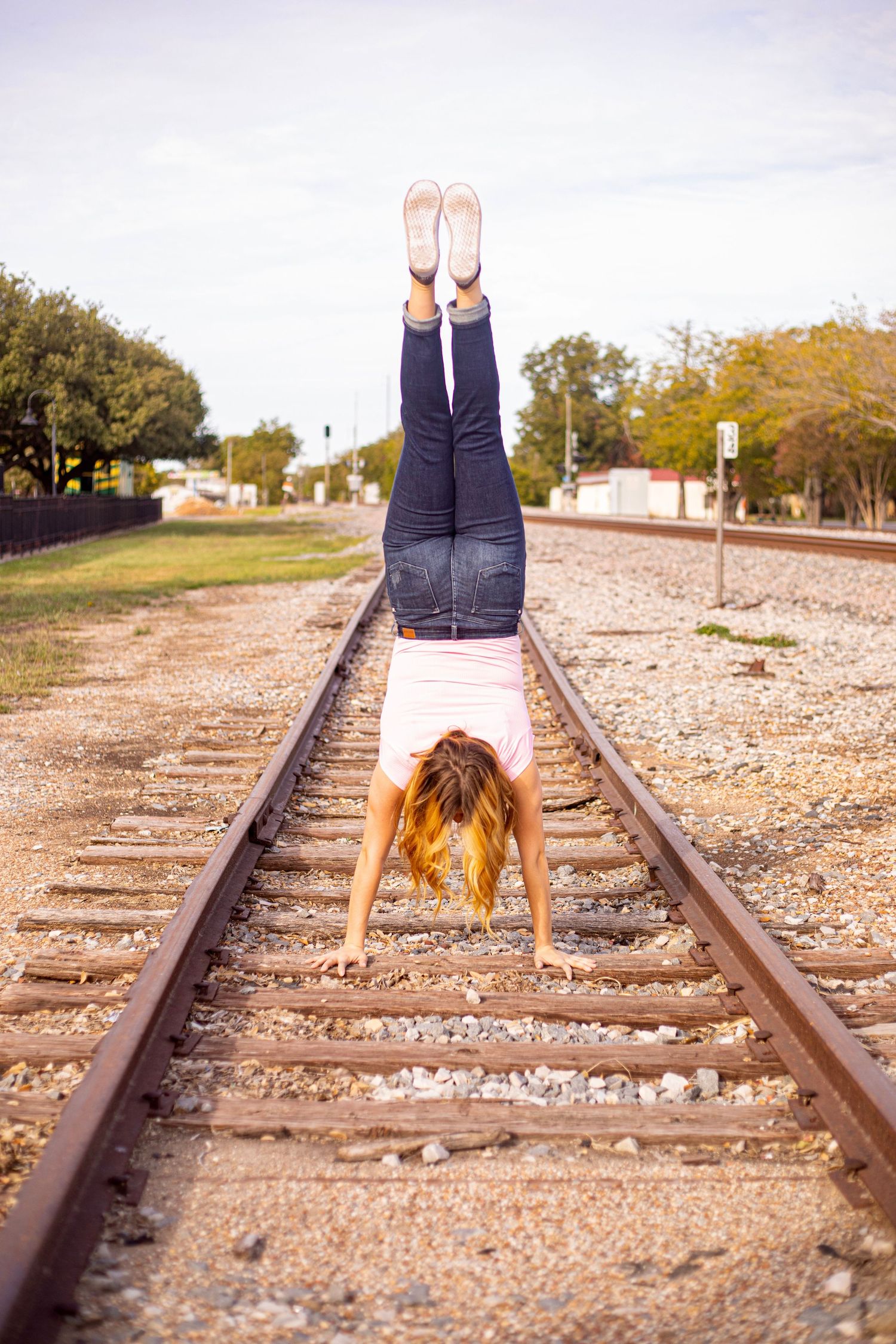 Creative portrait lying on train tracks with legs raised in the air against rural backdrop.