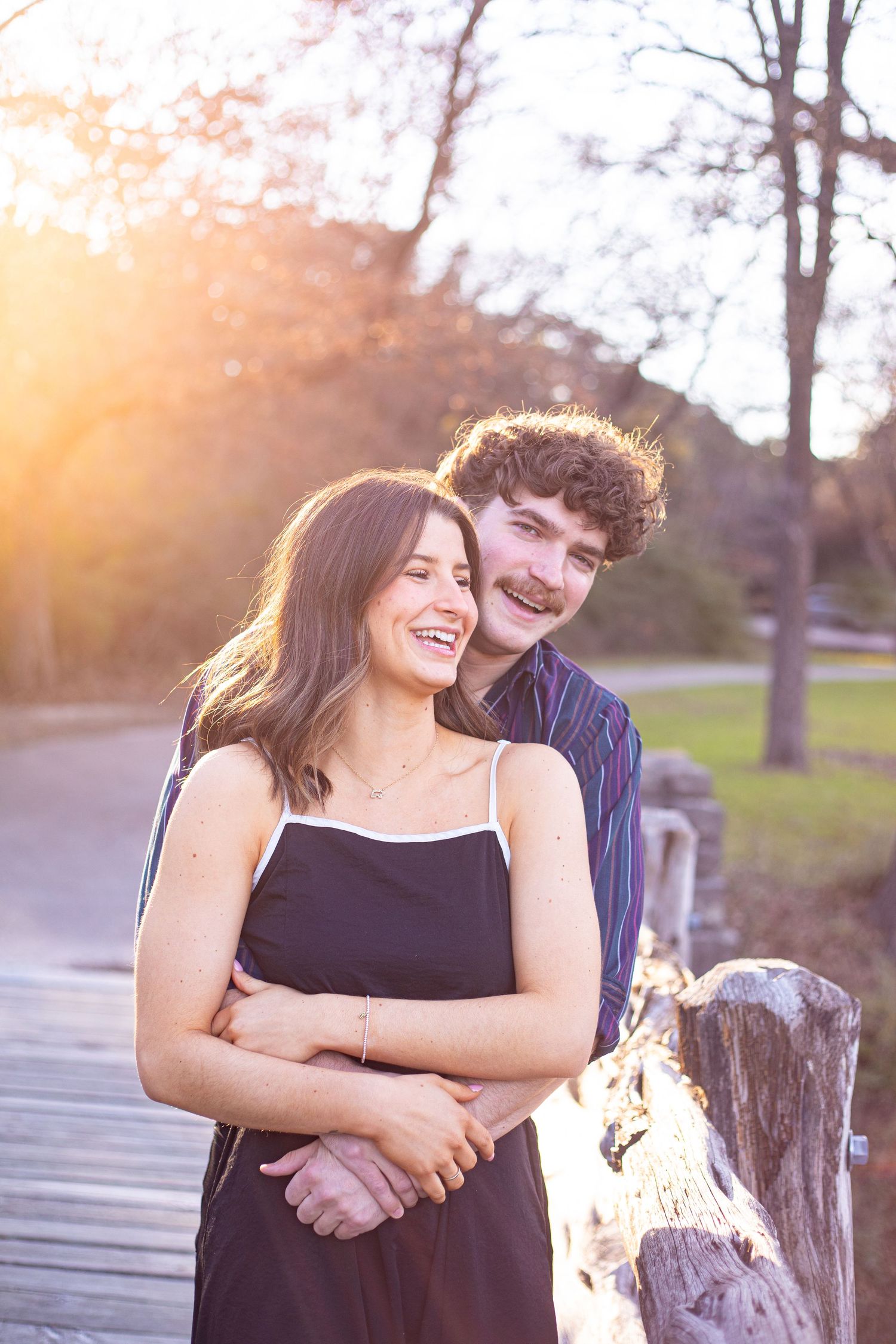 A couple shares a joyful moment together on a wooden boardwalk during golden hour.