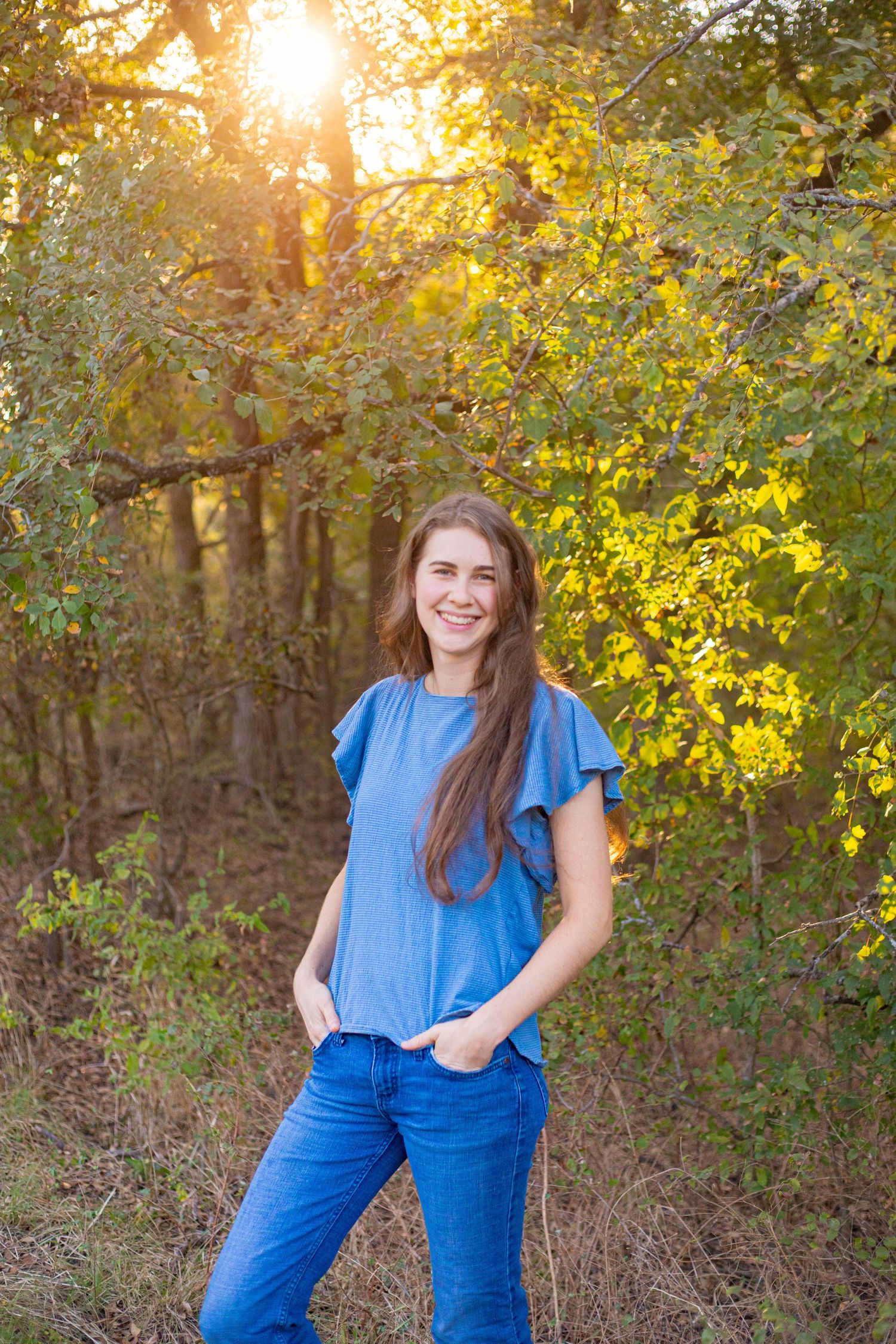Person in blue shirt standing against autumn foliage with golden sunlight.