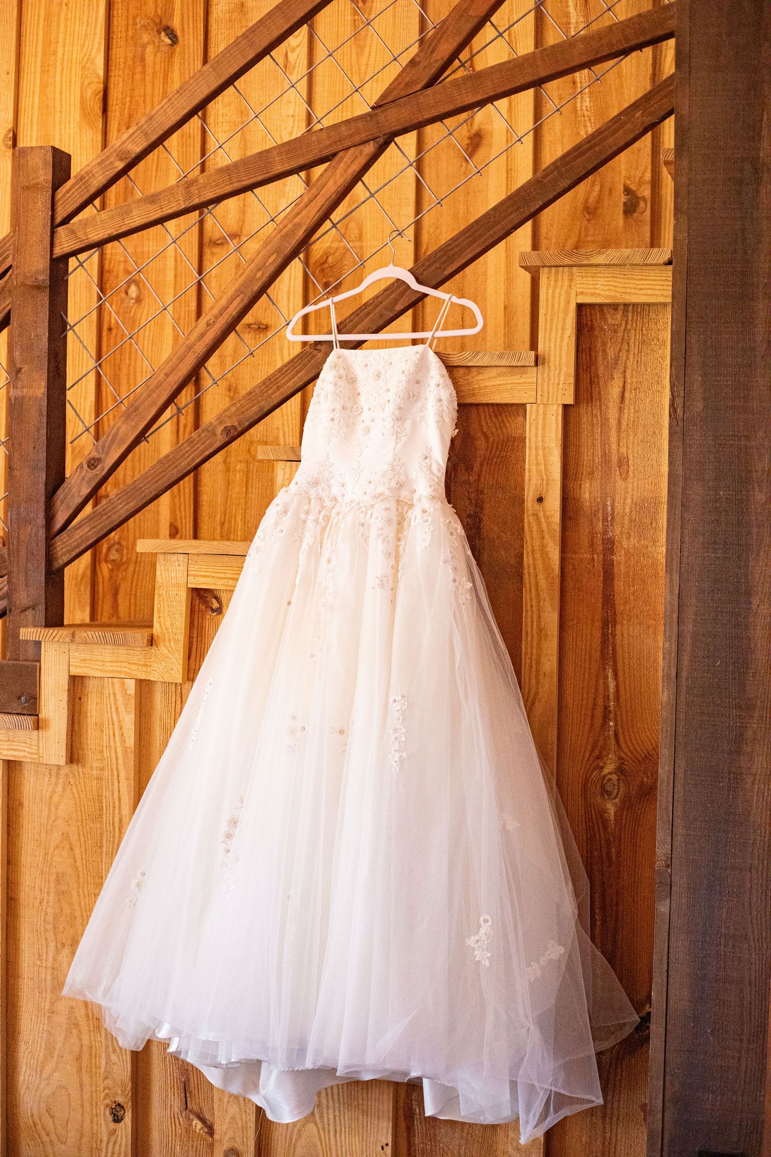 White tulle flower girl dresses hanging in rustic wooden barn setting.