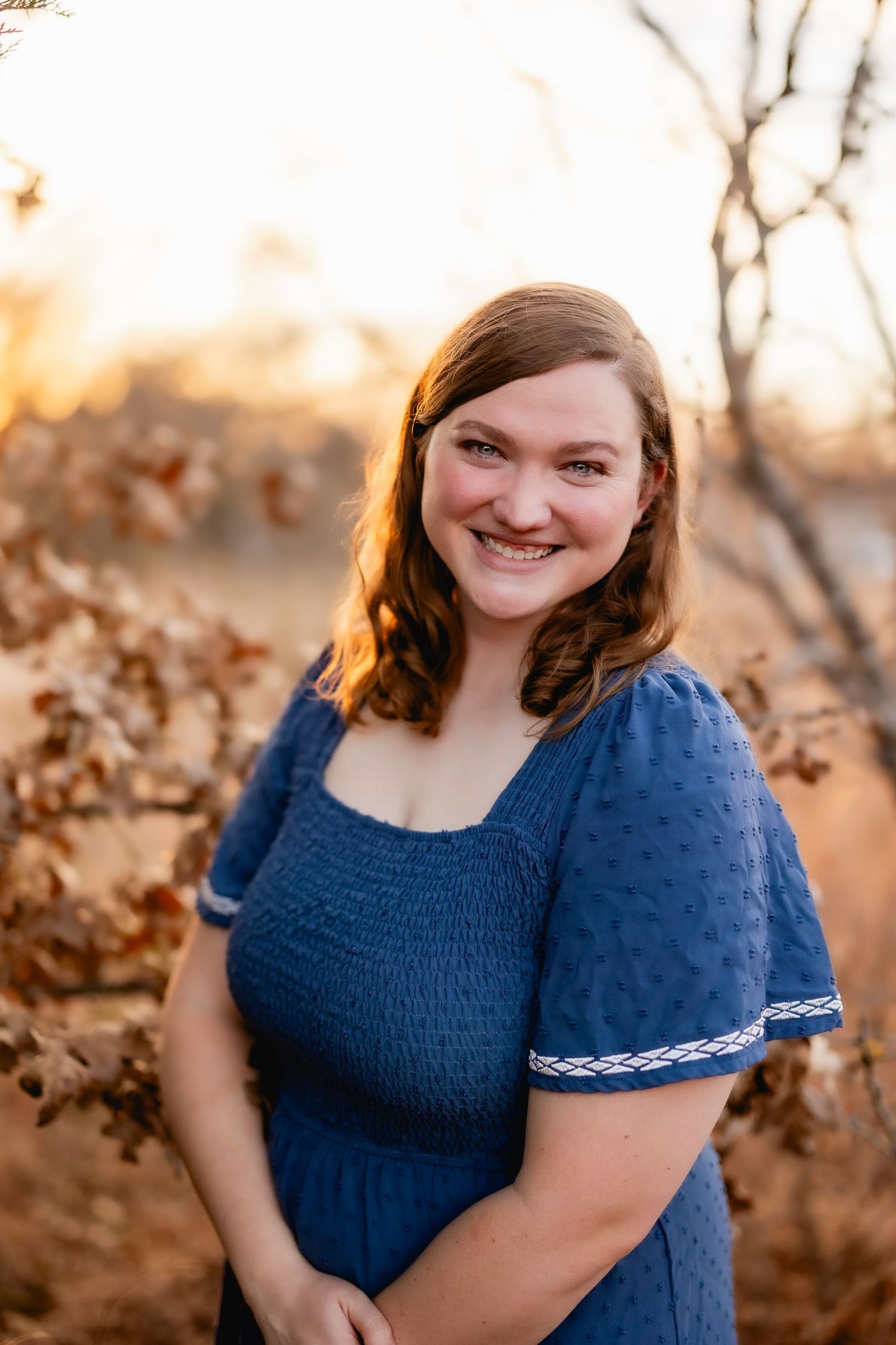 Woman in navy blue dress smiling warmly during sunset portrait session.