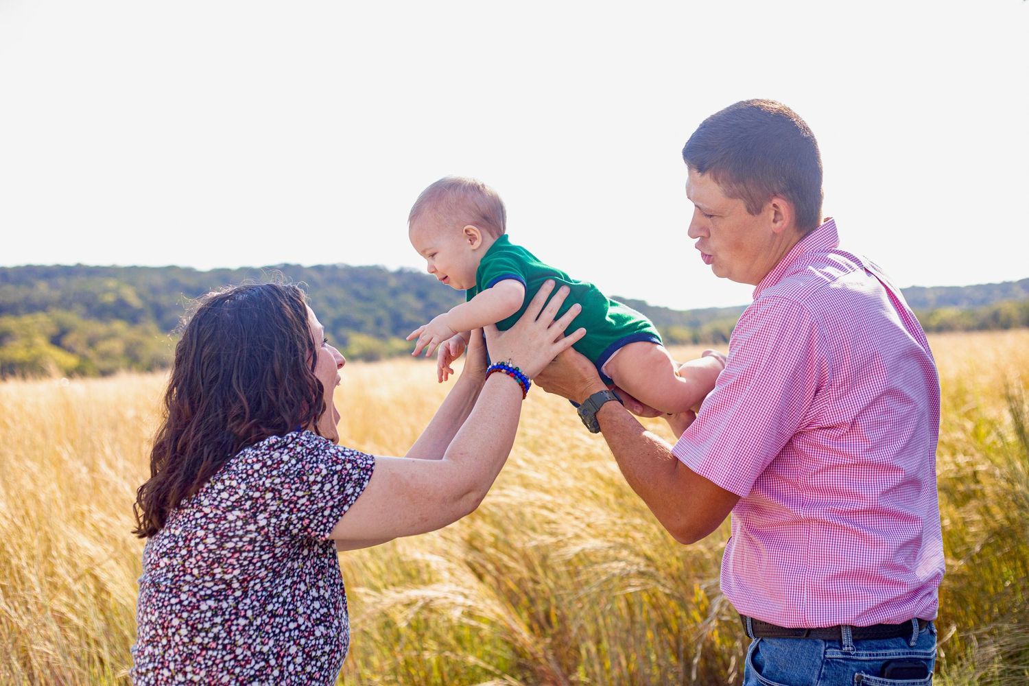 A family plays together in a sun-drenched field of tall grass.