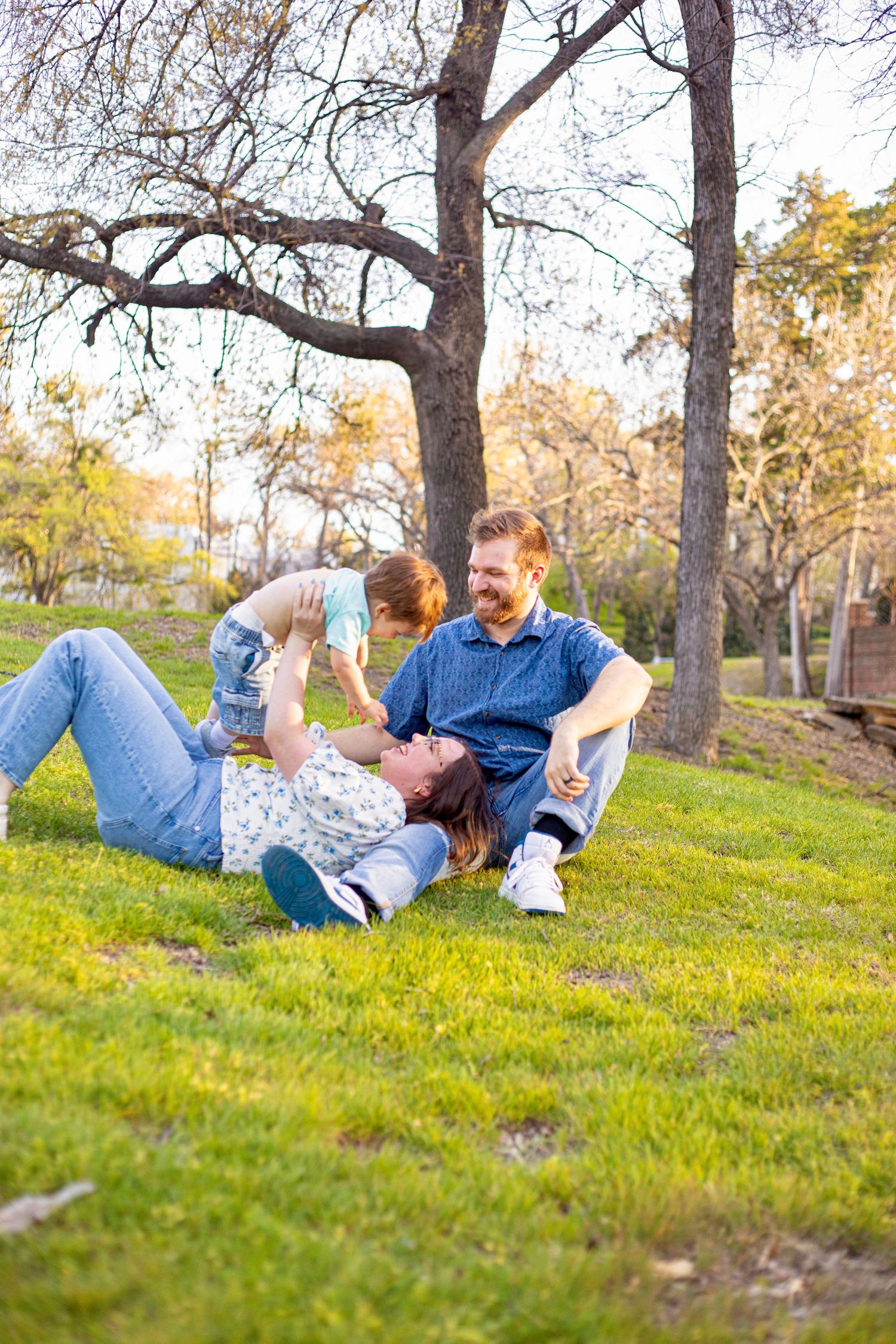 Family lying on green grass slope having fun during outdoor photoshoot.