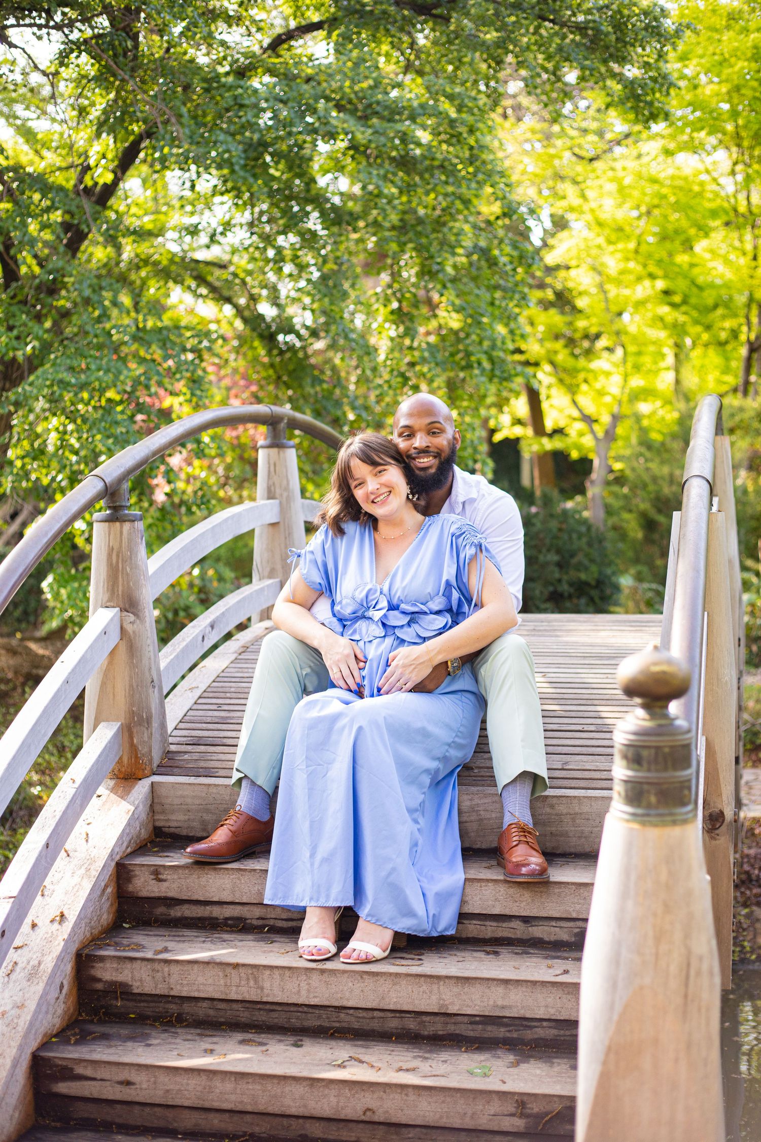 Romantic couple photos on wooden bridge surrounded by lush green trees.
