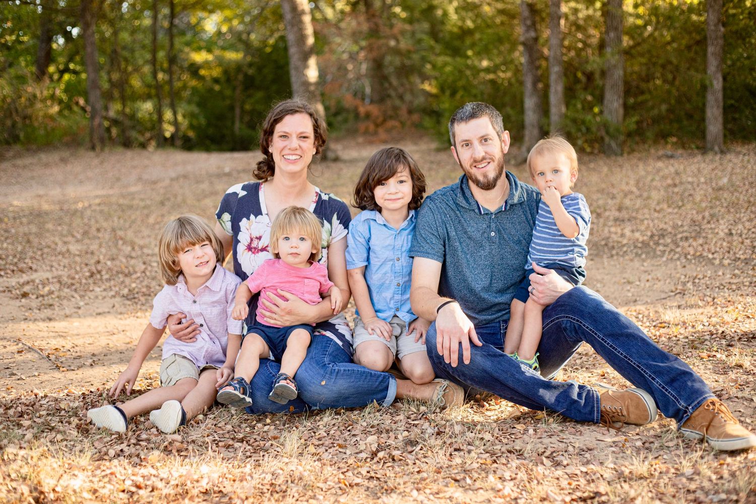 Family sitting together on fallen leaves in an autumn forest setting.