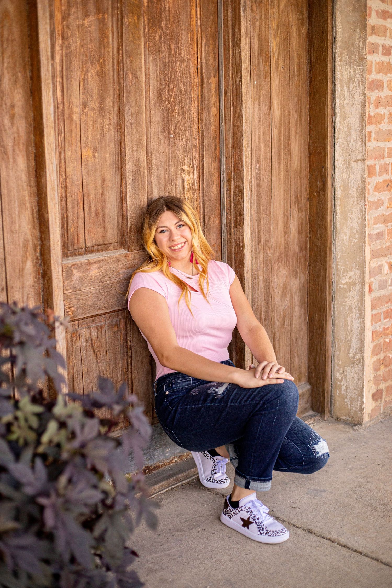 Portrait series against rustic wooden wall with casual pink top and jeans.