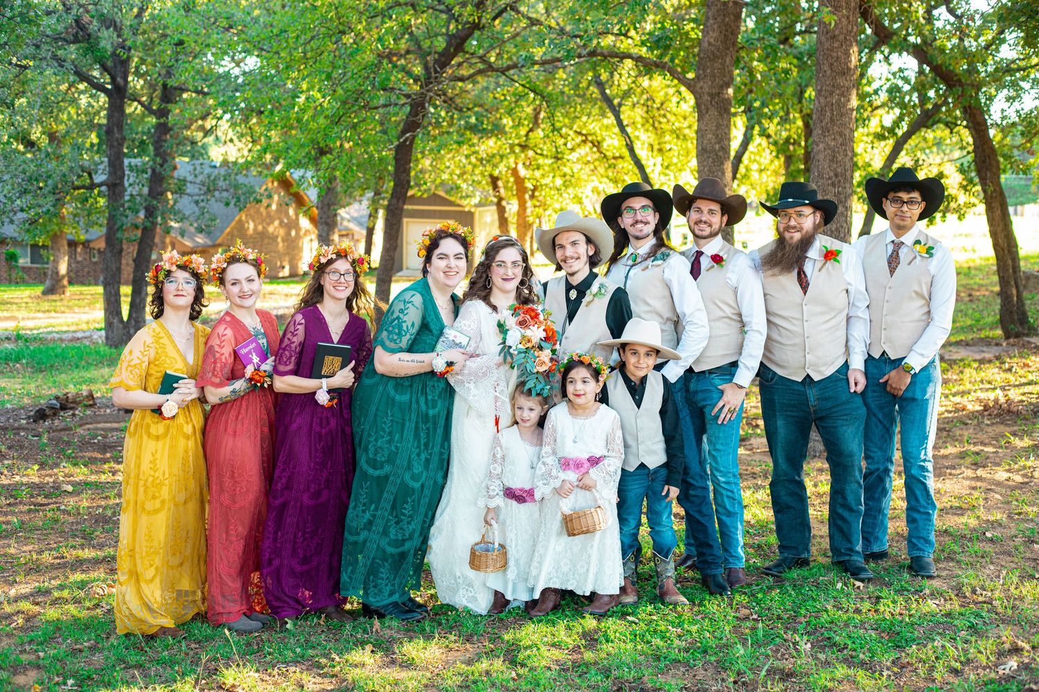 Wedding party in colorful dresses and western attire posing together in outdoor garden setting.