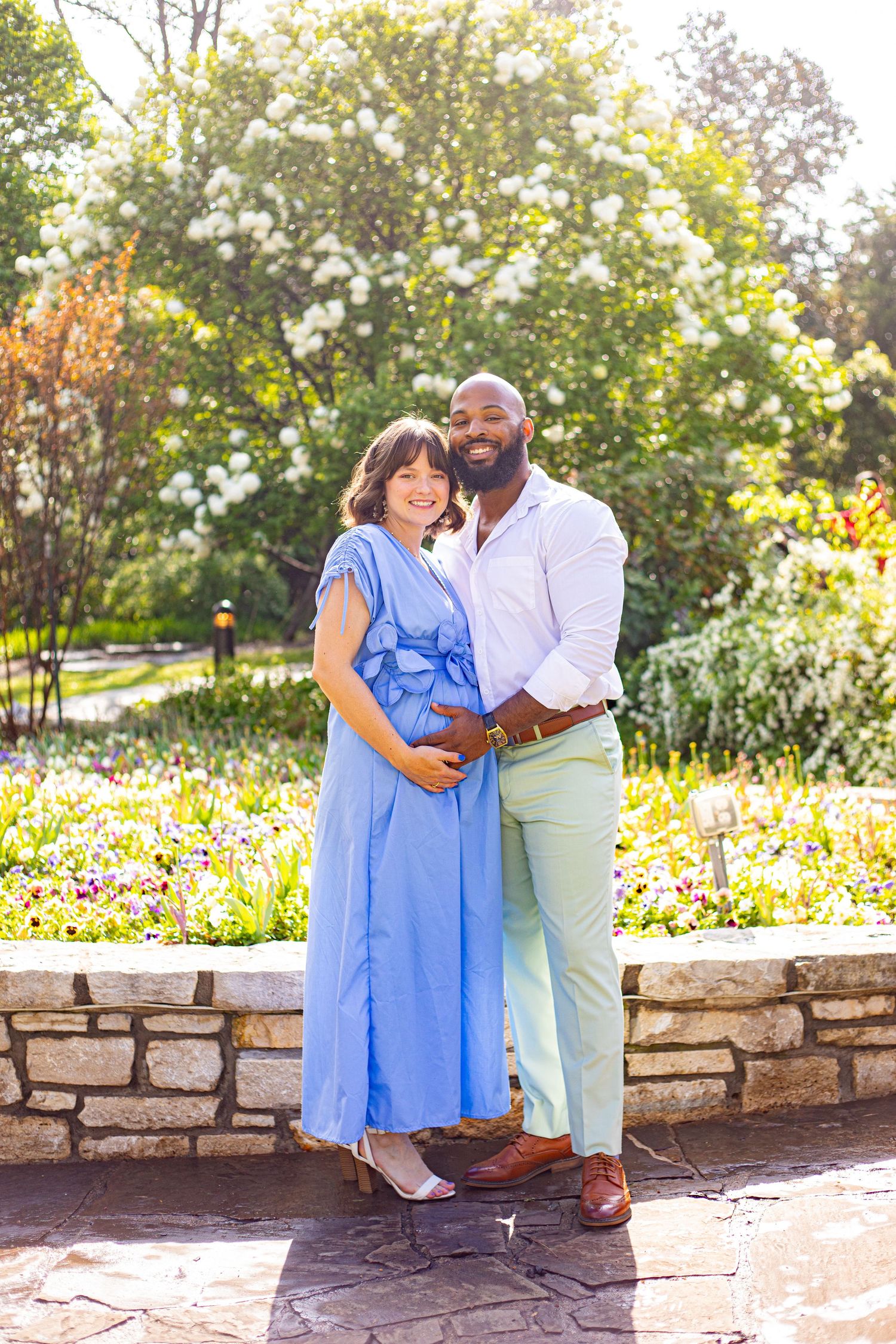 Romantic couple posing together by stone wall in garden with woman in blue dress and man in mint pants.