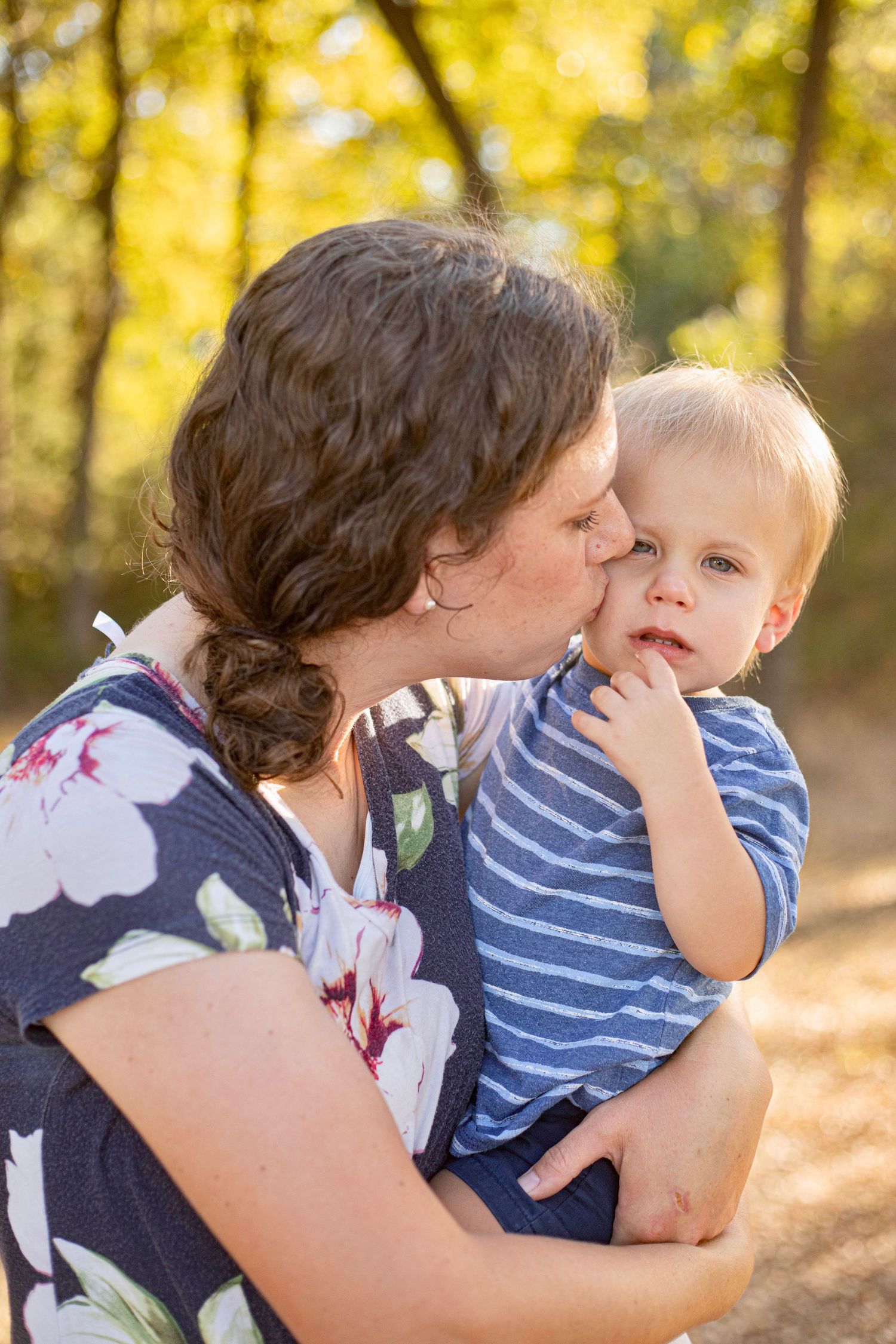Tender moment captured in golden sunlight between parent and child in wooded setting.