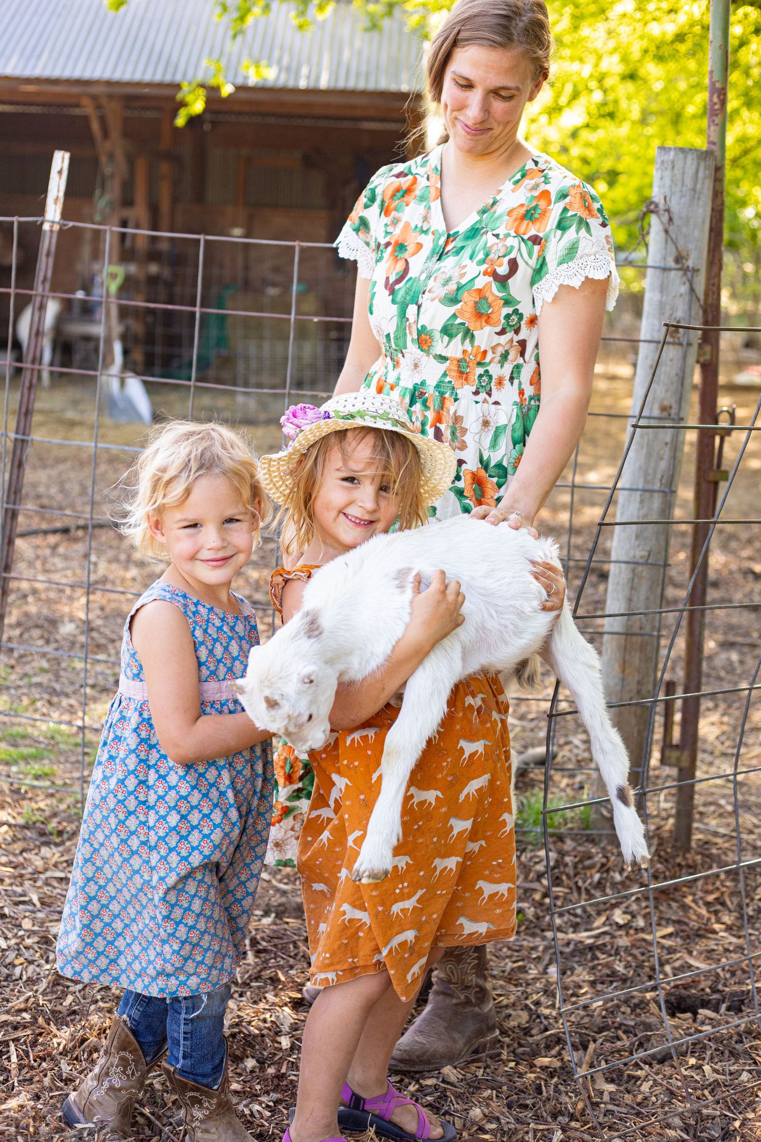 Children and adults interacting with a small white goat near a wooden fence outdoors.