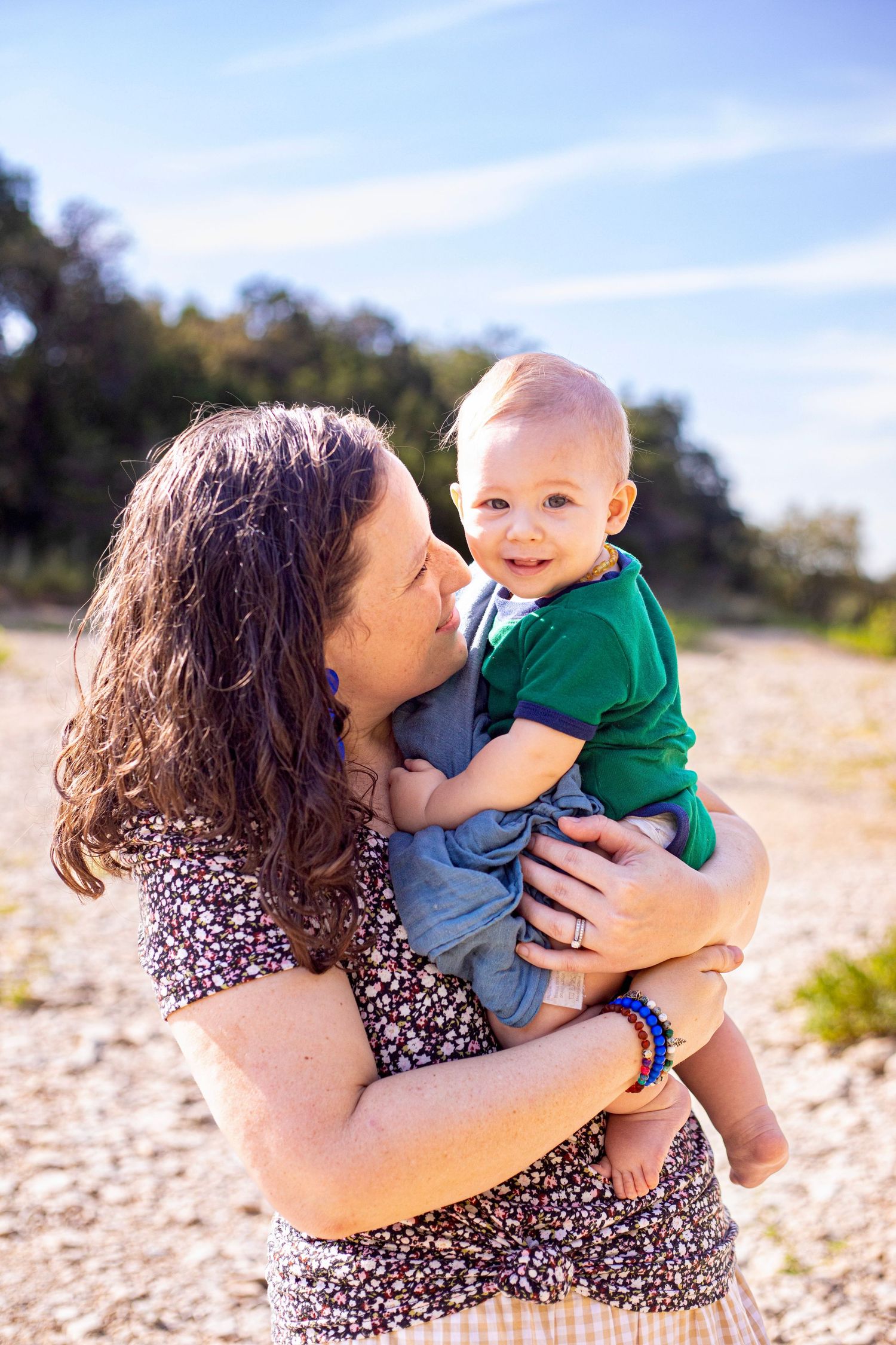 Mother and young child share tender moment on rocky beach during sunset.
